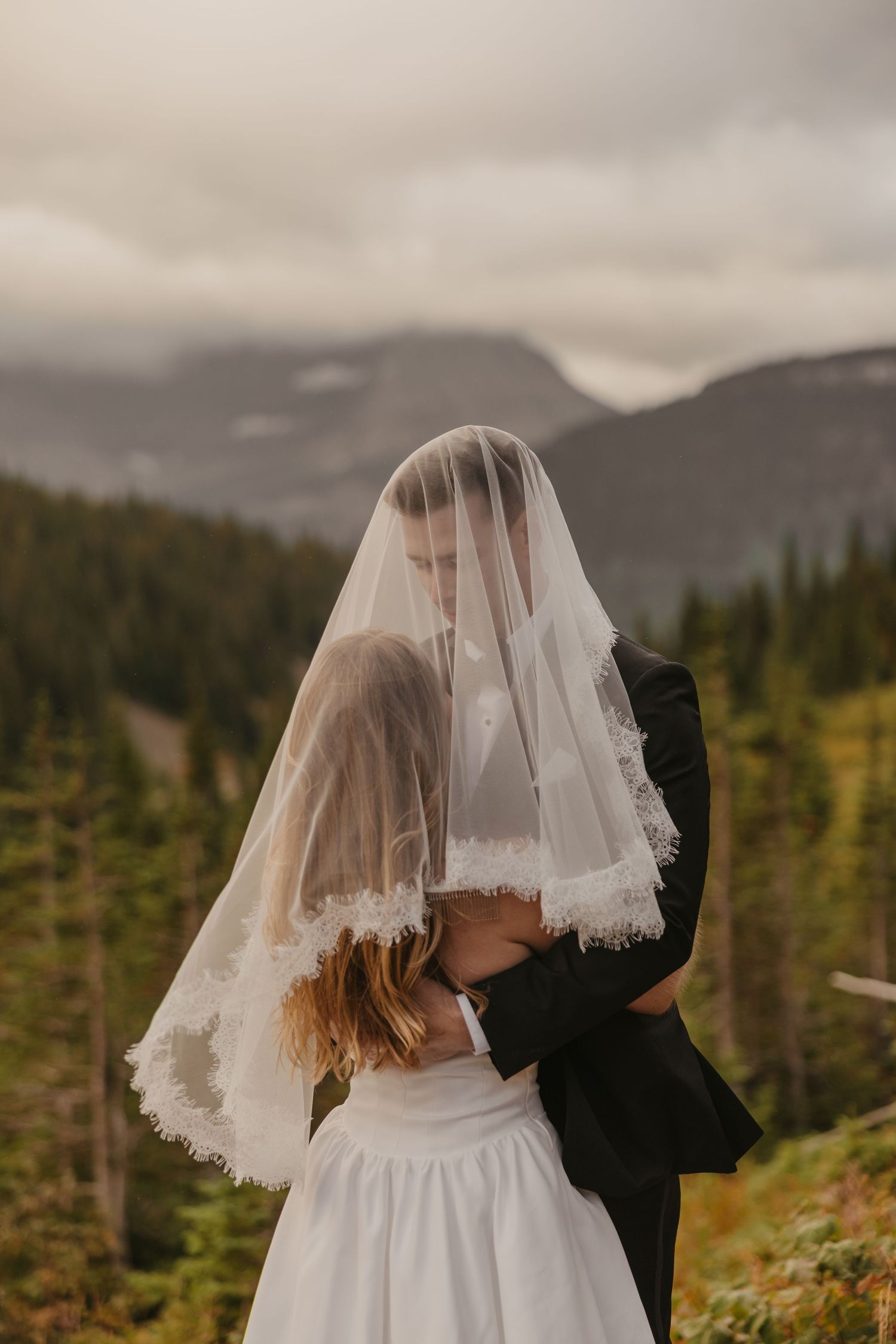 Bride and groom under veil in Glacier National Park captured by local Elopement Photographer in Glacier on a moody cloudy elopement day