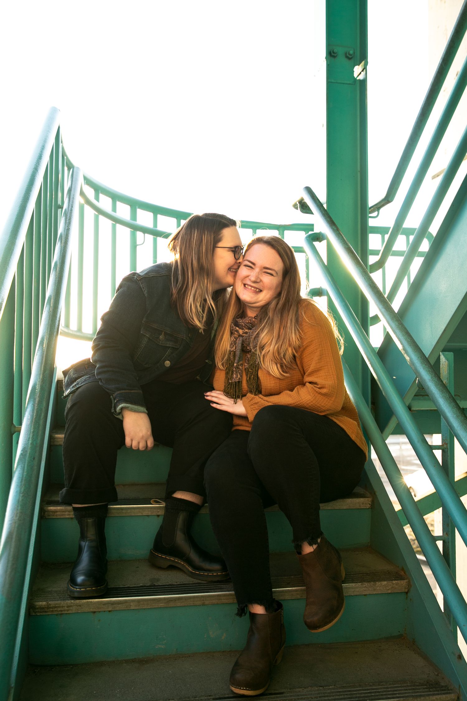 Two people sharing a tender moment together while sitting on green metal stairs in warm sunlight.