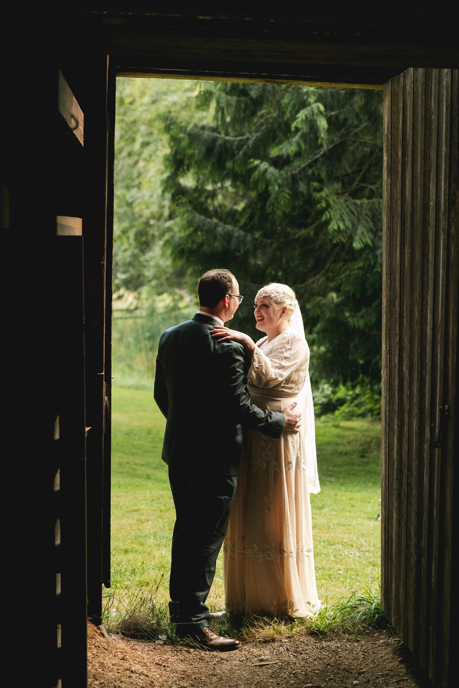 An intimate wedding scene framed through a dark doorway shows a couple in traditional attire standing on a garden path.