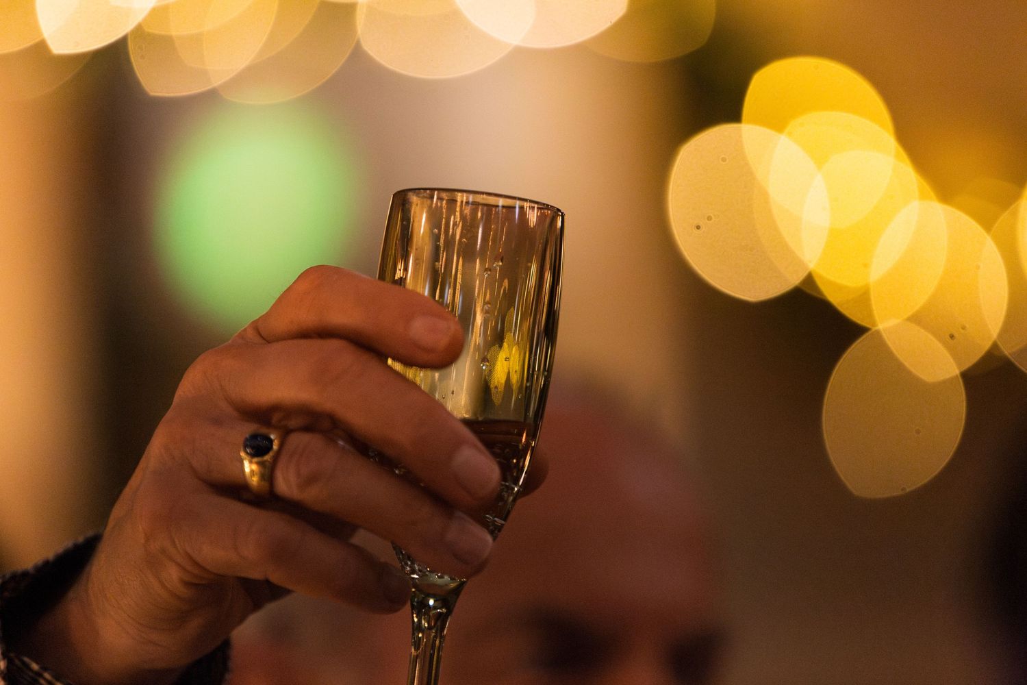 A hand holding a champagne glass with sparkling gold bokeh lights in the background creating a festive atmosphere.