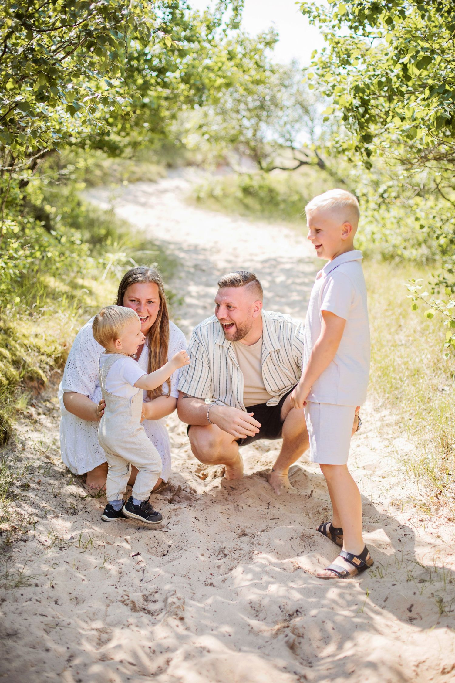 A playful family scene unfolds in a sequence of candid moments on a sandy beach path surrounded by greenery.