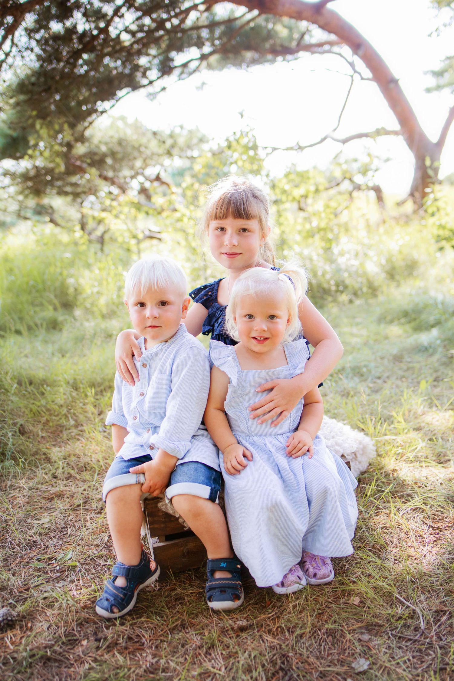 Young children in matching light blue outfits sit together under a tree branch in a natural outdoor setting.