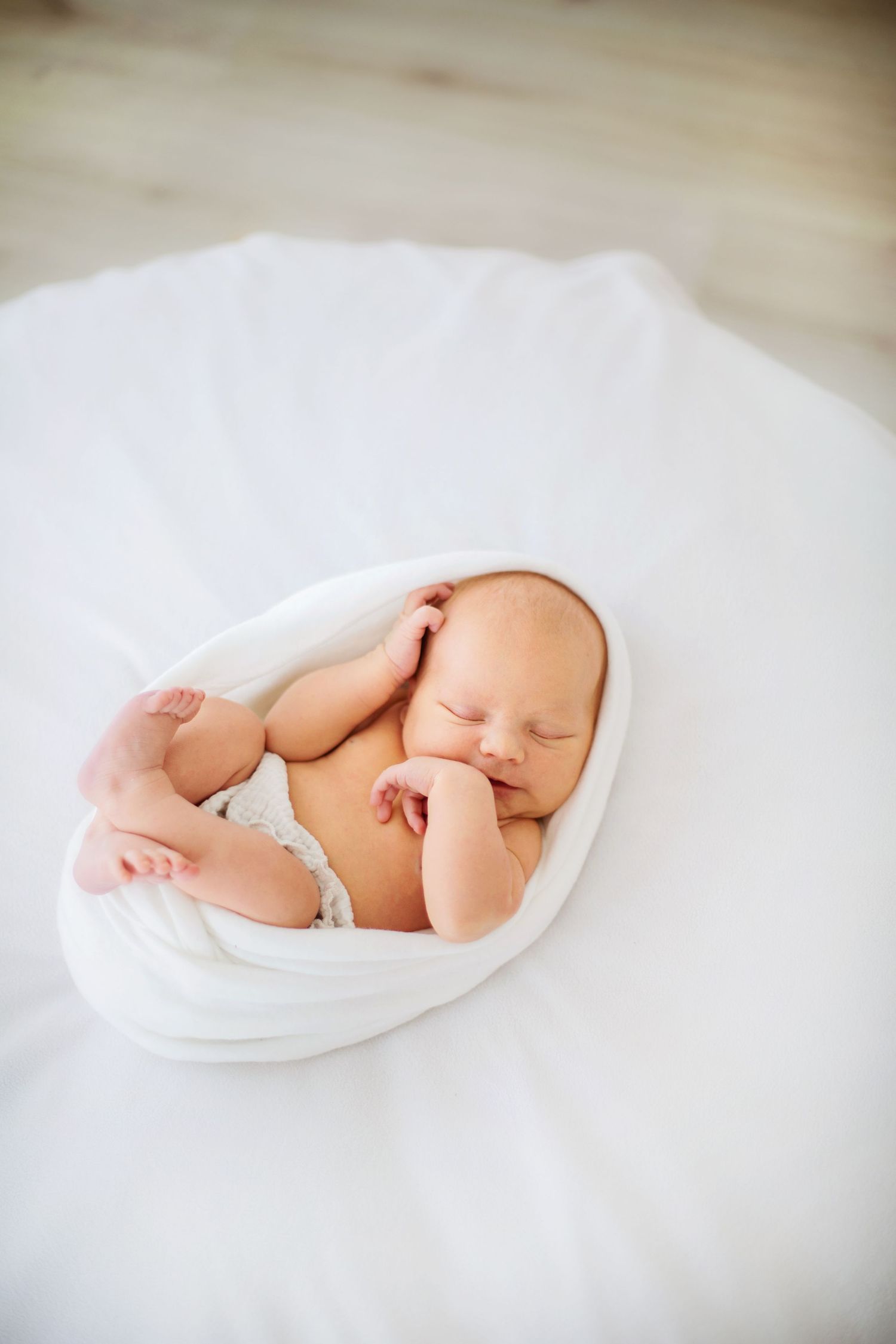 Newborn baby sleeping peacefully on soft white blanket in minimalist artistic photography series.
