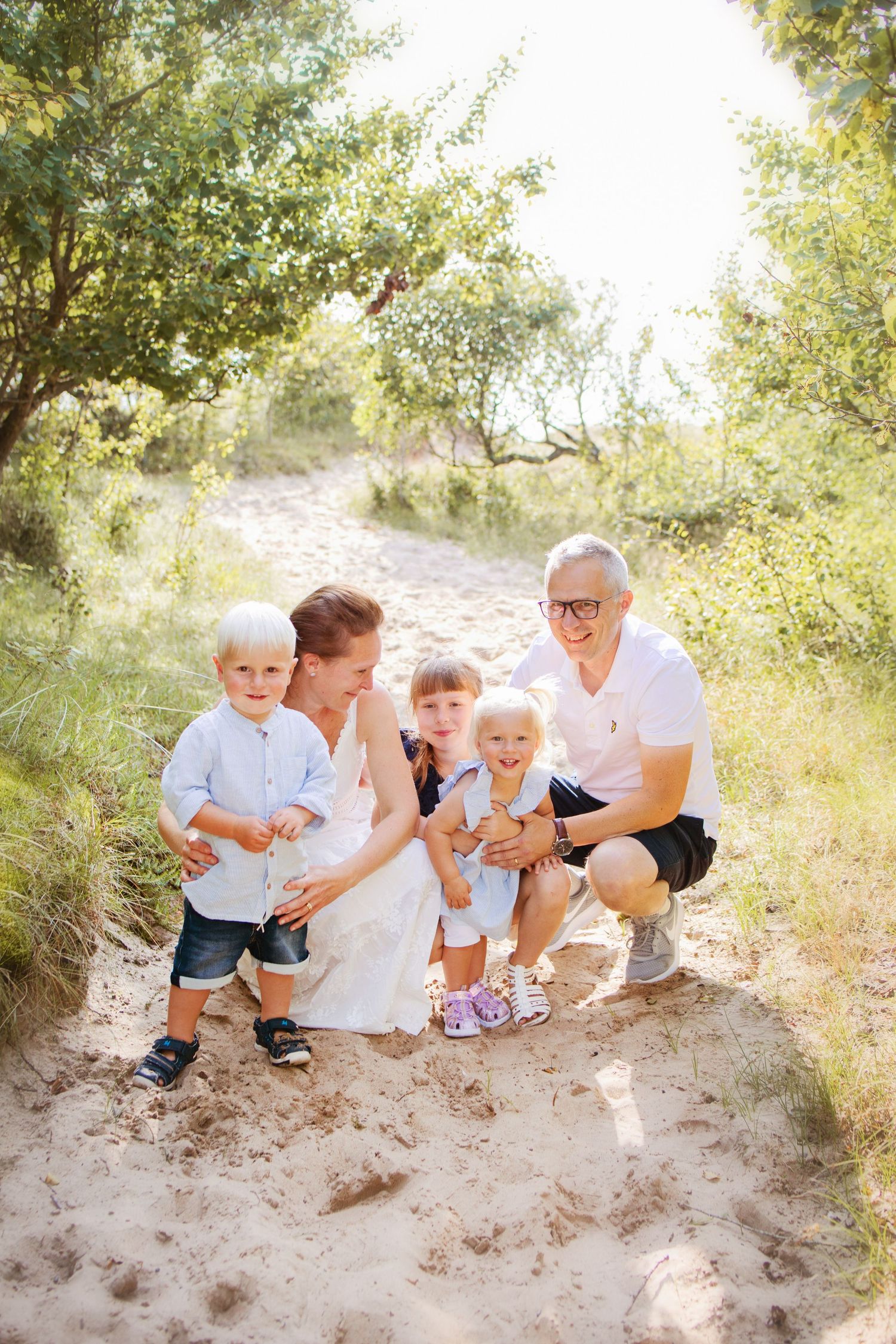 A family sits together on a sandy hill surrounded by green foliage on a sunny day.