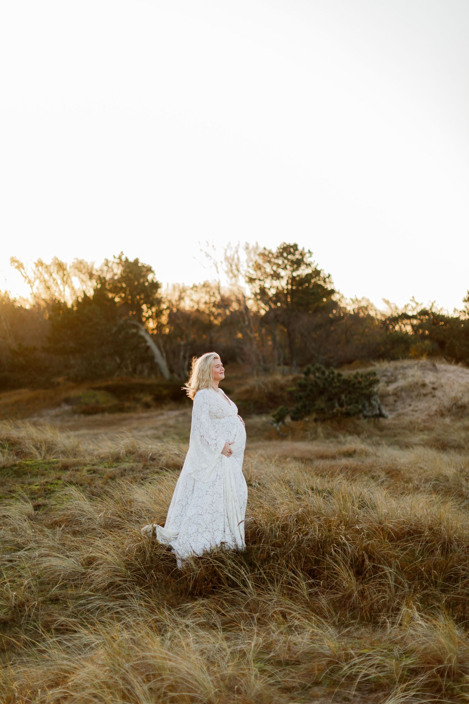 A figure in a flowing white dress stands in golden sunlit grass against a sunset backdrop.