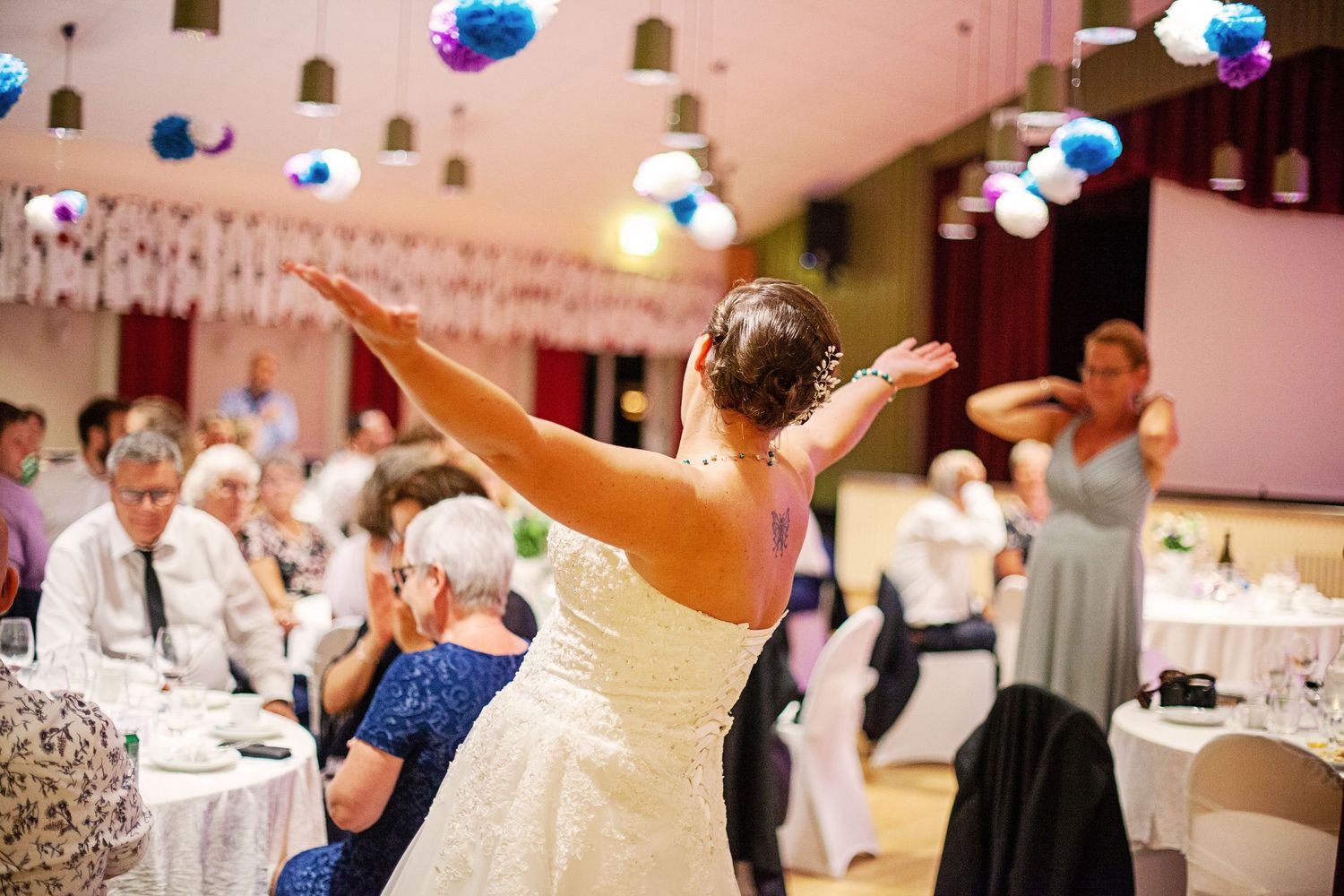 Bride in white gown tossing bouquet at elegant wedding reception with colorful decorations.