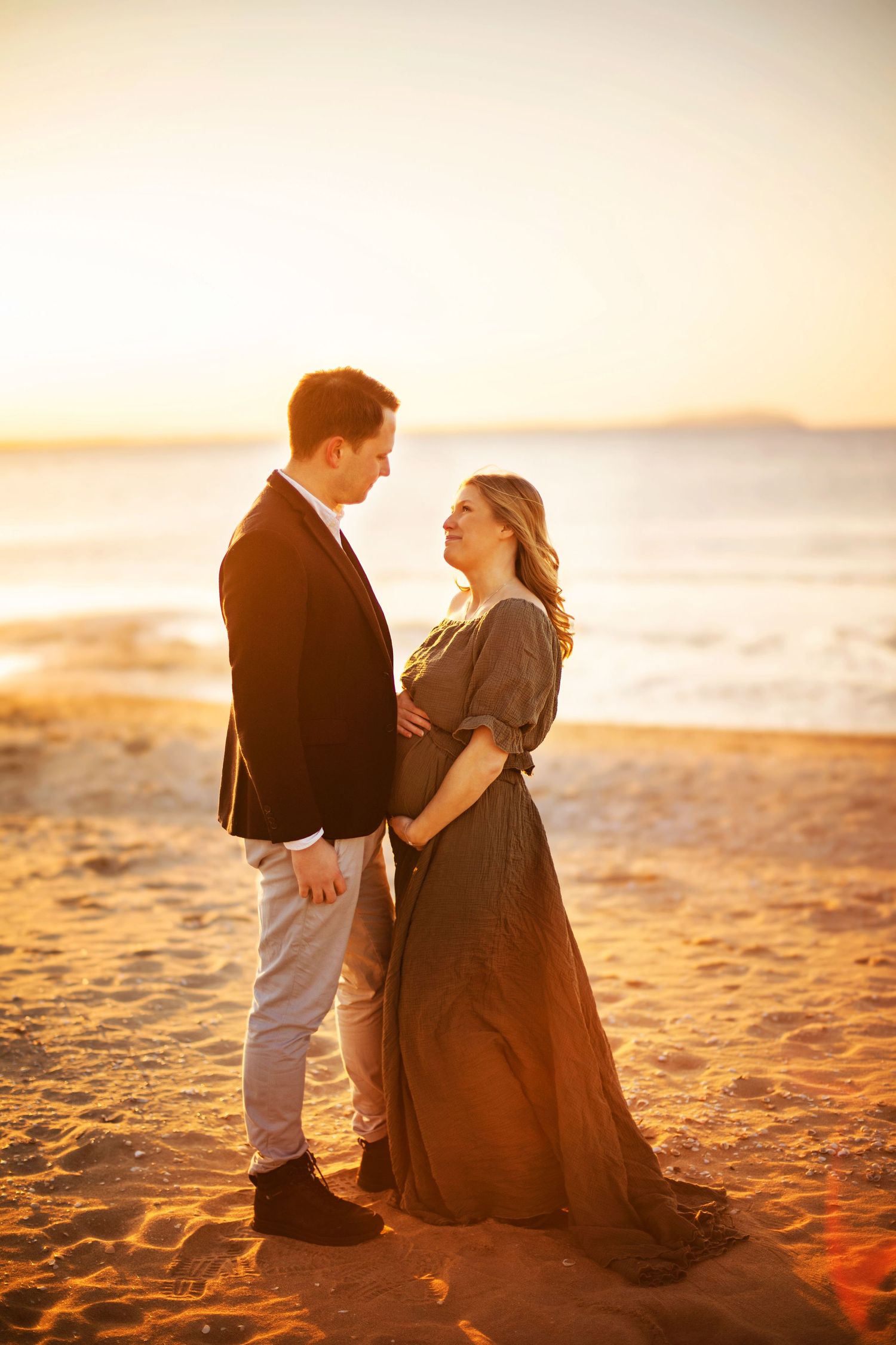 A couple shares a romantic moment on a sandy beach at sunset, silhouetted against the golden sky.