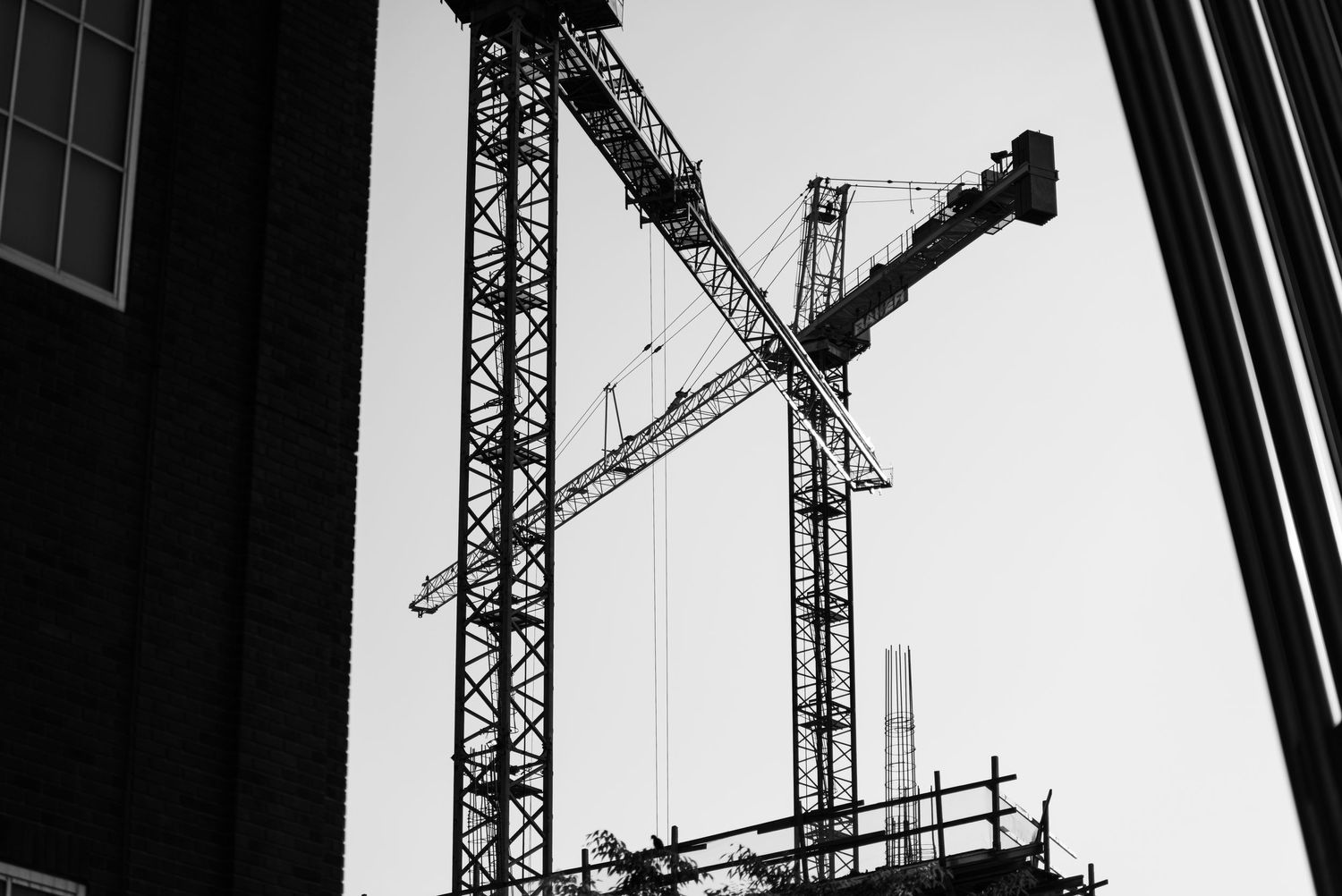 Construction site with tall industrial cranes silhouetted against sky in black and white photography.
