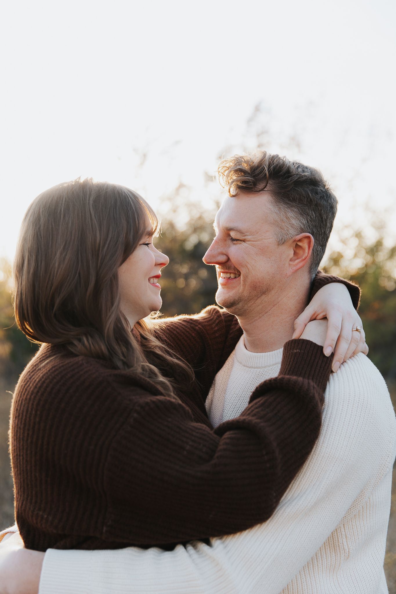 Happy couple in sweaters embracing and smiling at each other in autumn sunlight.