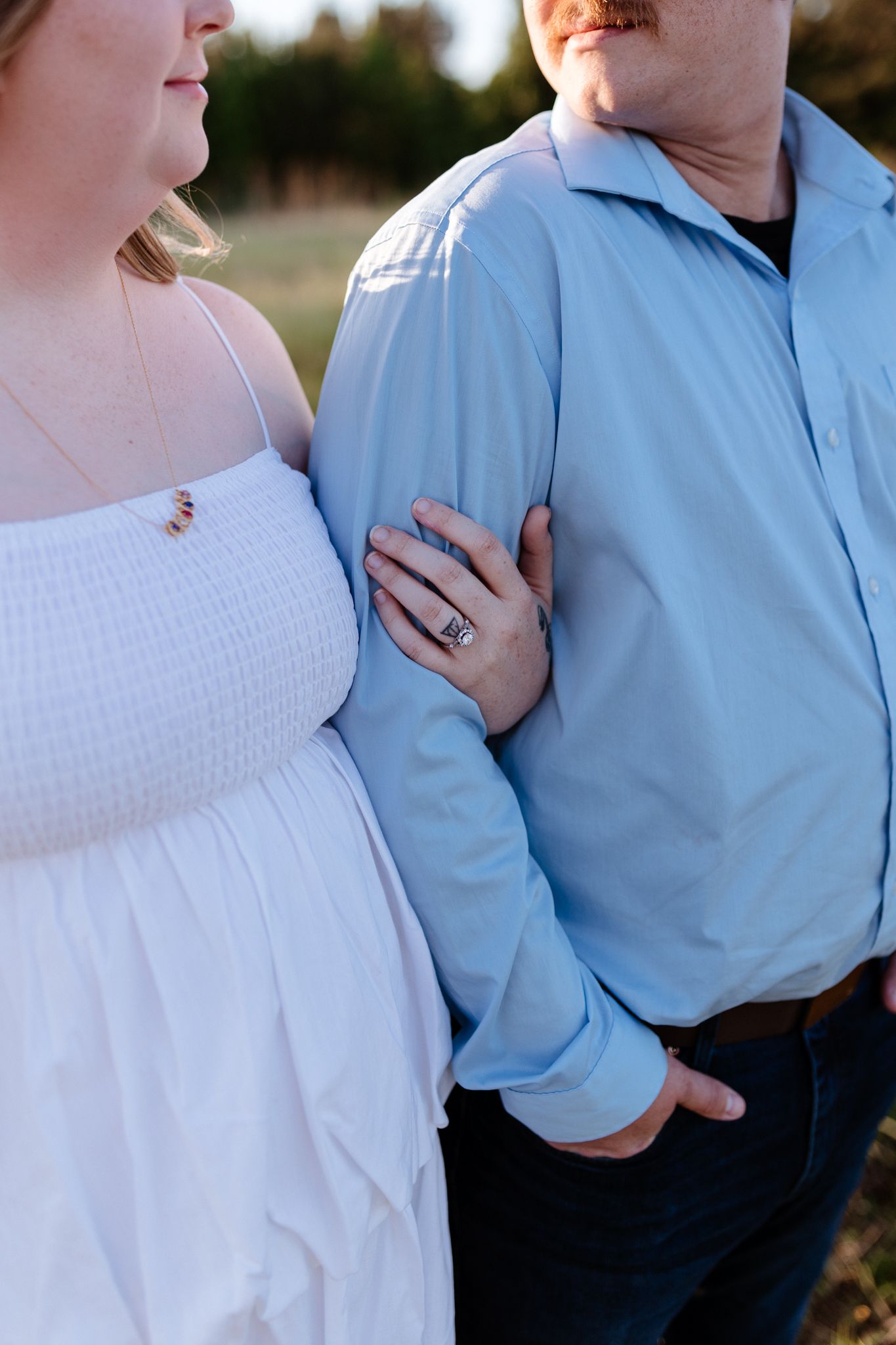 Close-up of couple embracing, woman's hand with engagement ring resting on man's light blue shirt.