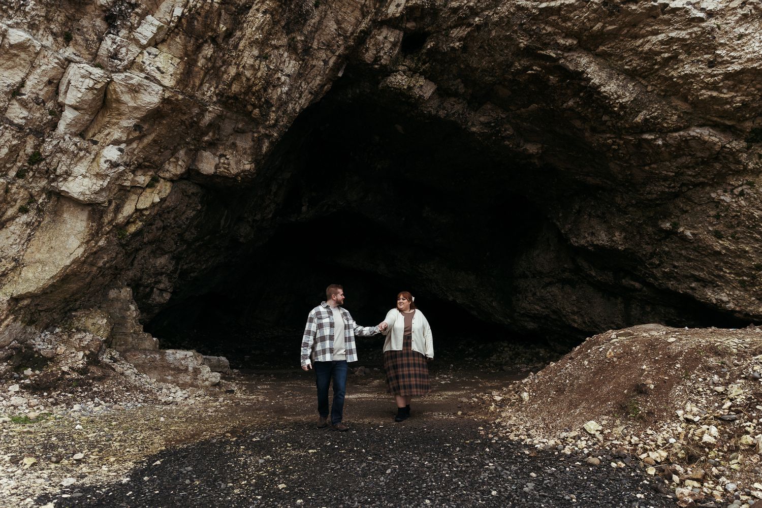 Couple holding hands walking out of dramatic rocky cave entrance together.