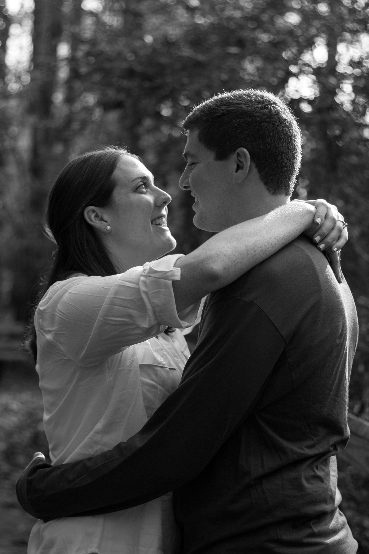 Black and white photo of couple embracing and gazing at each other in a forest setting.