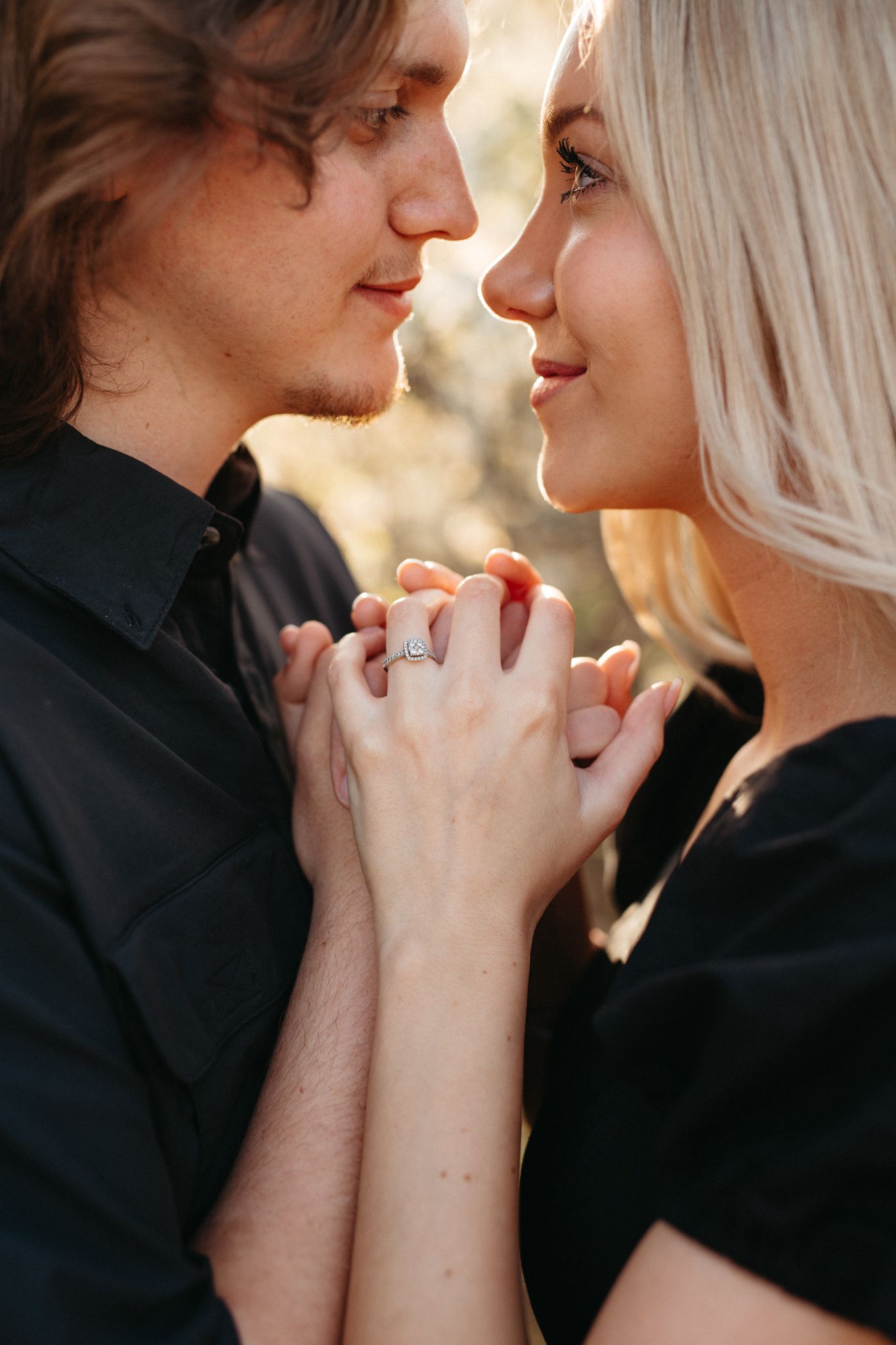 Close up of couple holding hands with engagement ring almost kissing outdoors.