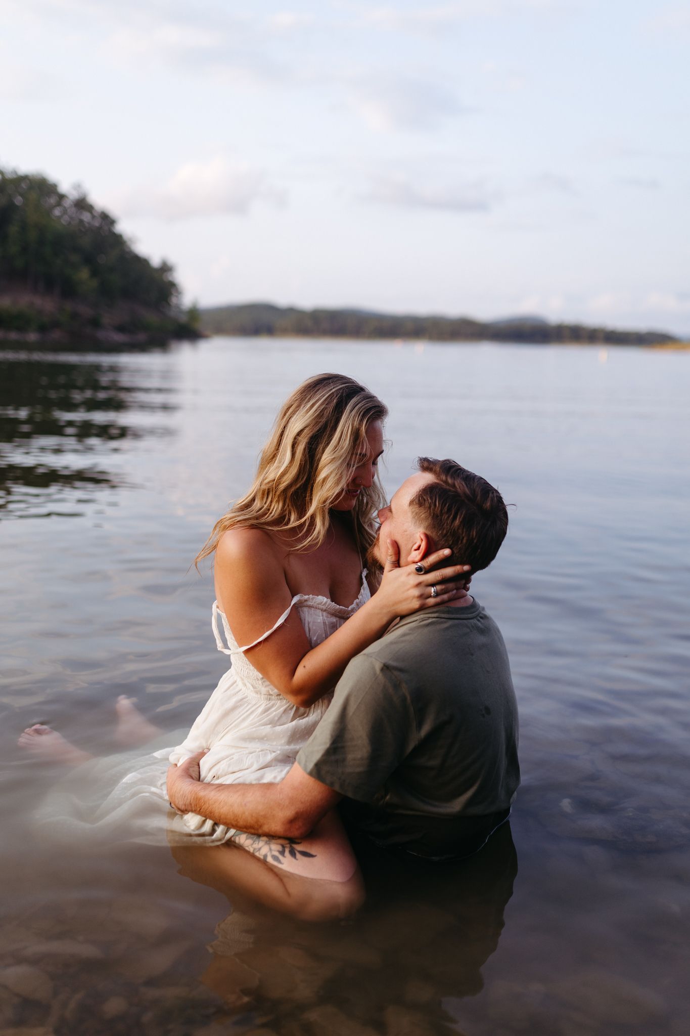 Romantic couple embracing and almost kissing while sitting in shallow lake water.