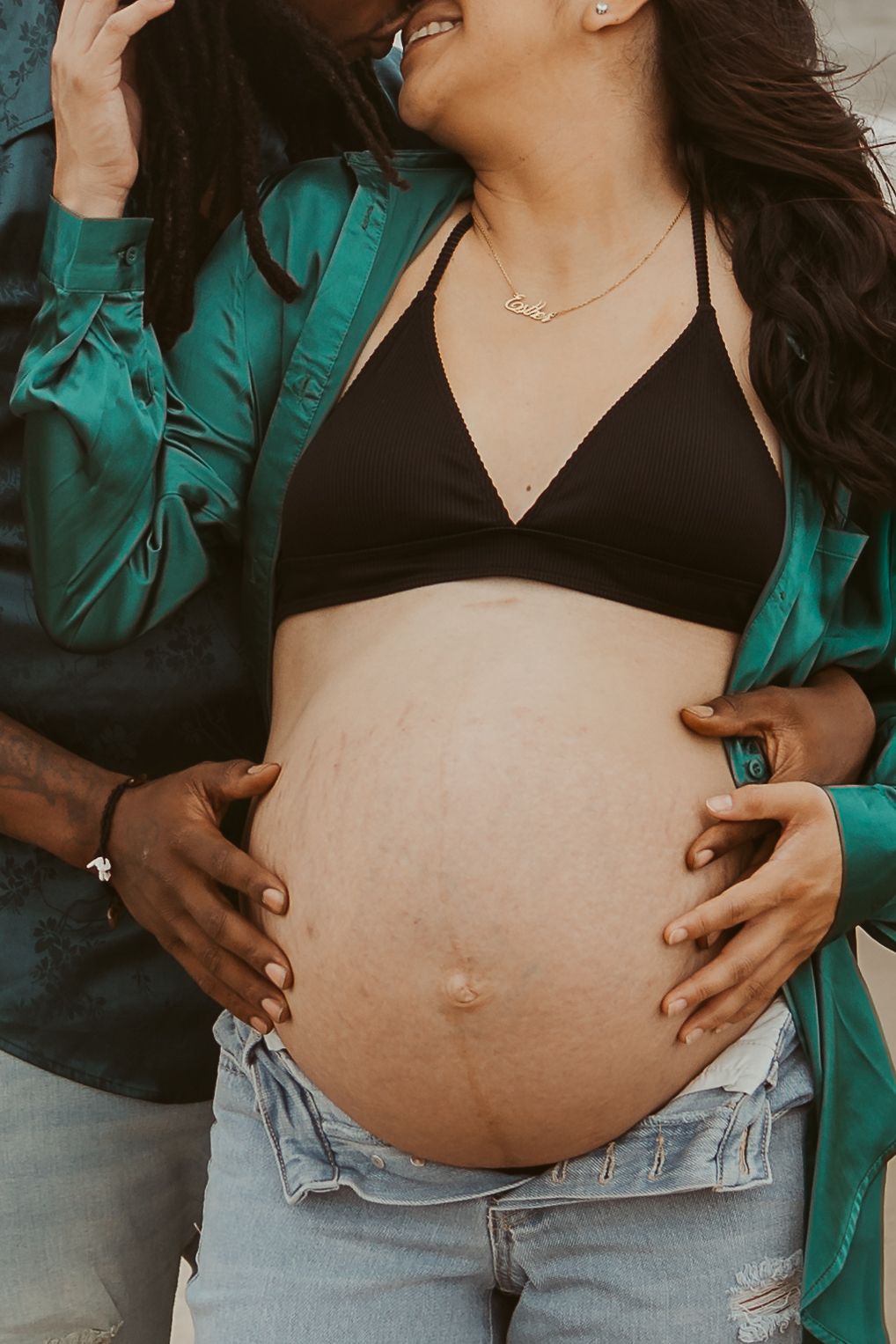 Close-up of pregnant womans baby bump with partners hands cradling belly during beach shoot.