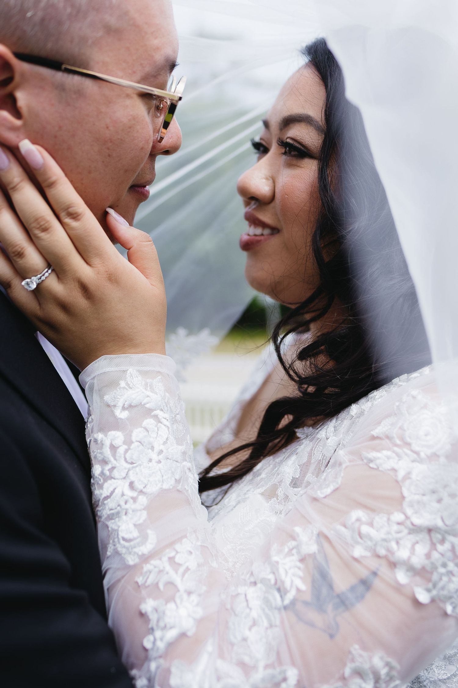 Bride tenderly holding grooms face under veil, sharing an intimate moment.