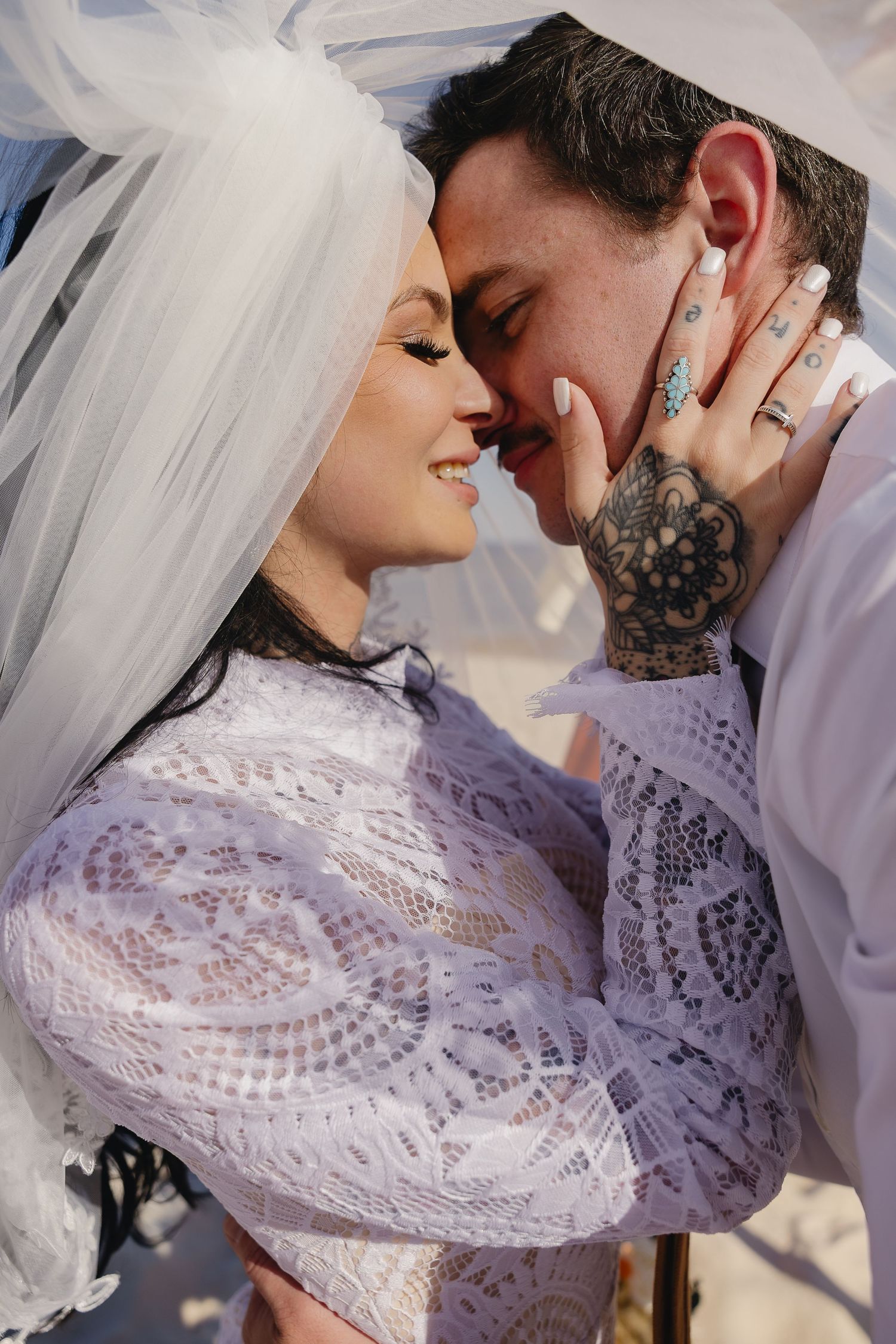 Bride and groom share an intimate moment under a veil on the beach at their wedding.