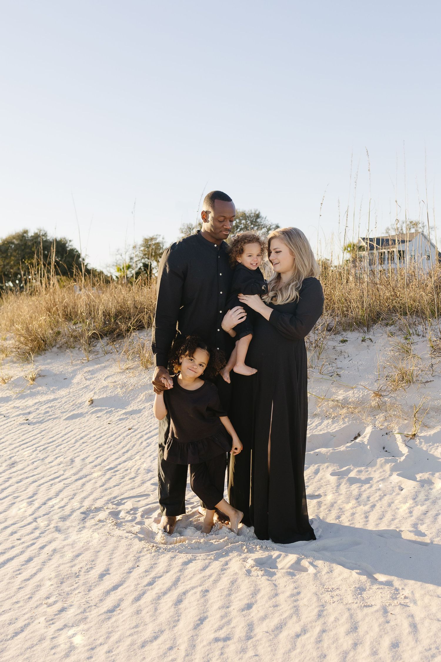 Loving family of four dressed in black posing together on white sand dunes.