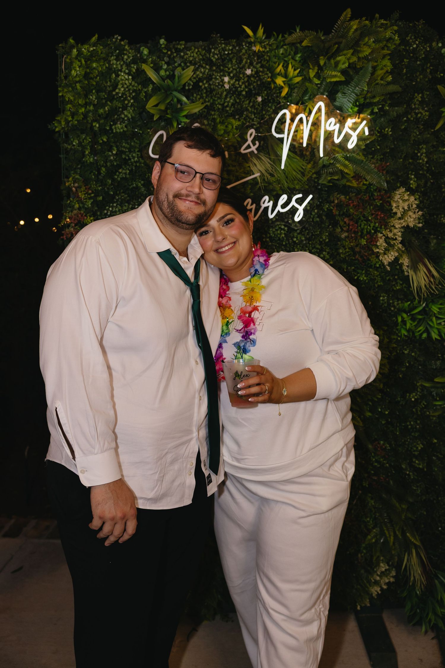 Couple posing together at wedding after-party in front of neon sign.