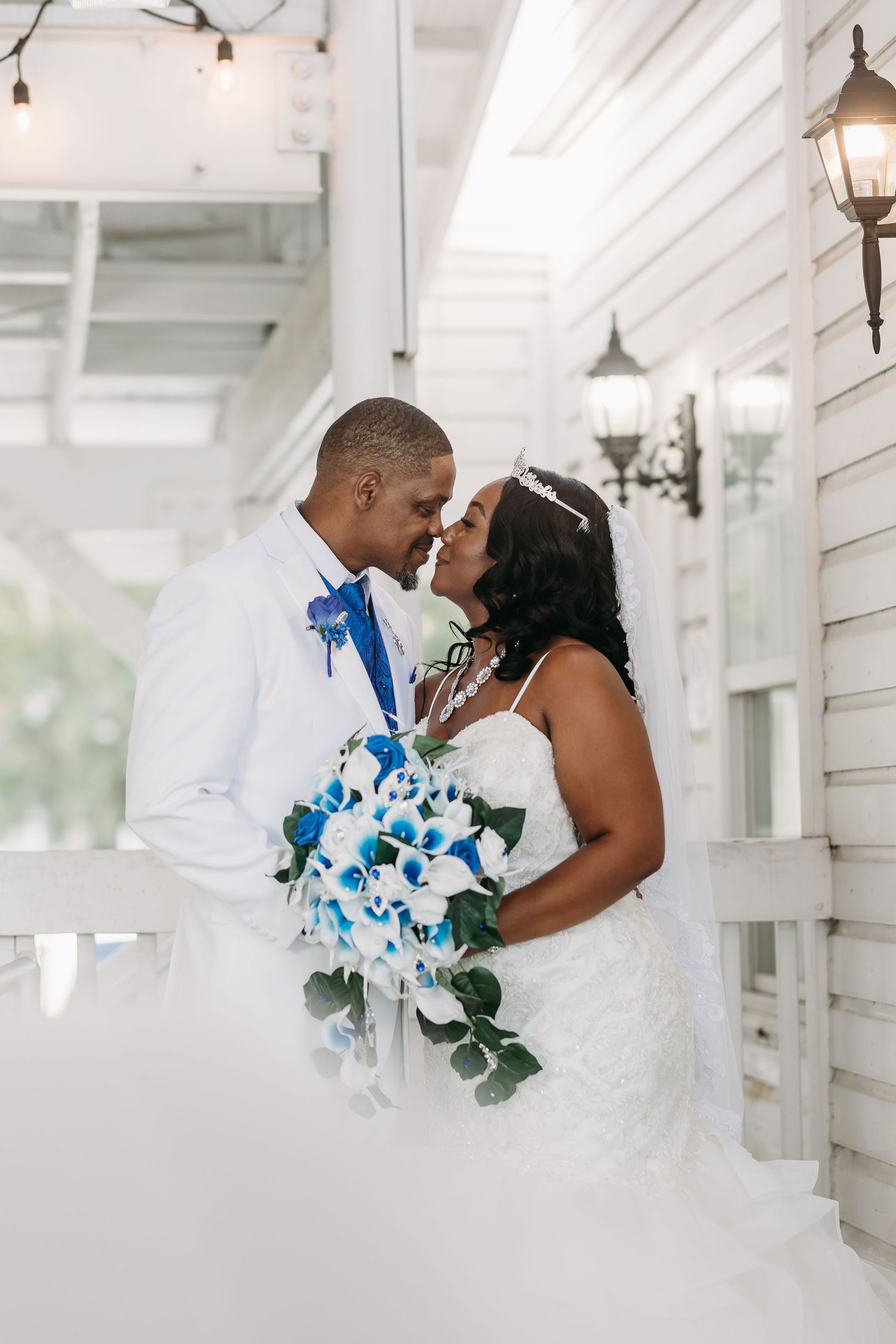 Bride and groom share romantic kiss on porch with blue and white cascading bouquet.
