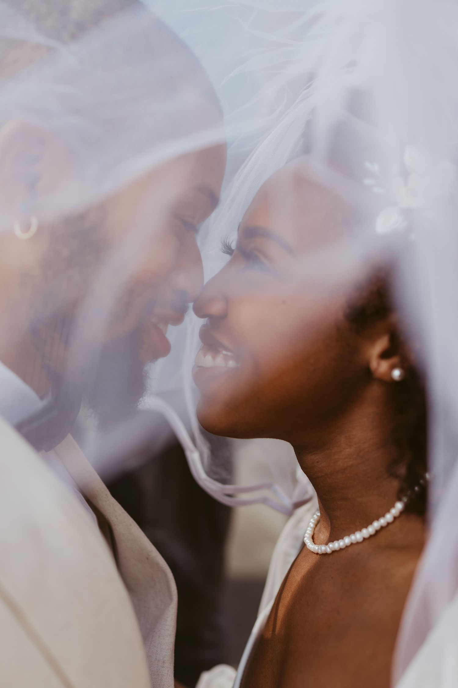 Close-up of smiling Black bride and groom touching foreheads under a sheer white wedding veil.