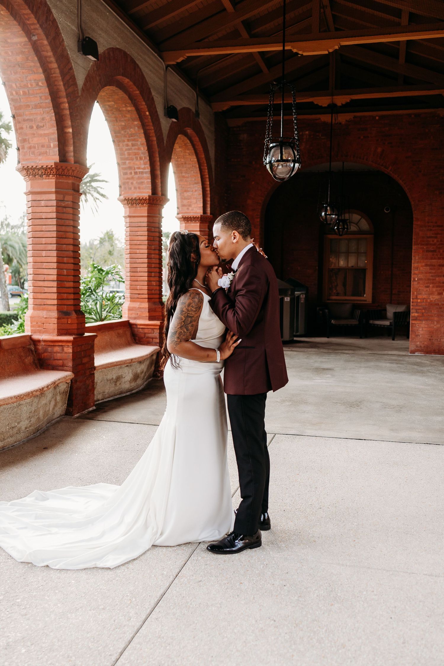 Bride and groom sharing a kiss under brick arches at an elegant wedding venue.