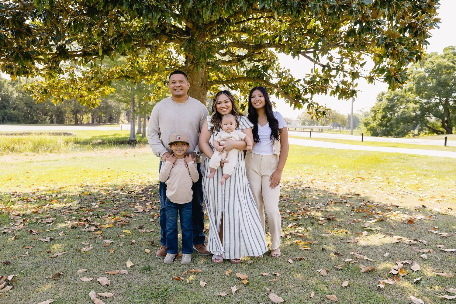 A family of four poses under a large tree in a scenic park during a fall photo session.