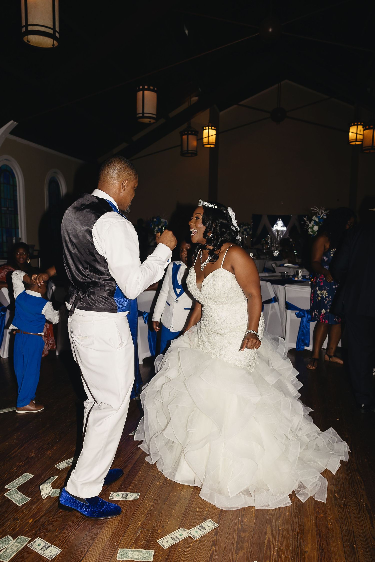 Bride and groom share first dance surrounded by guests with money on dance floor.