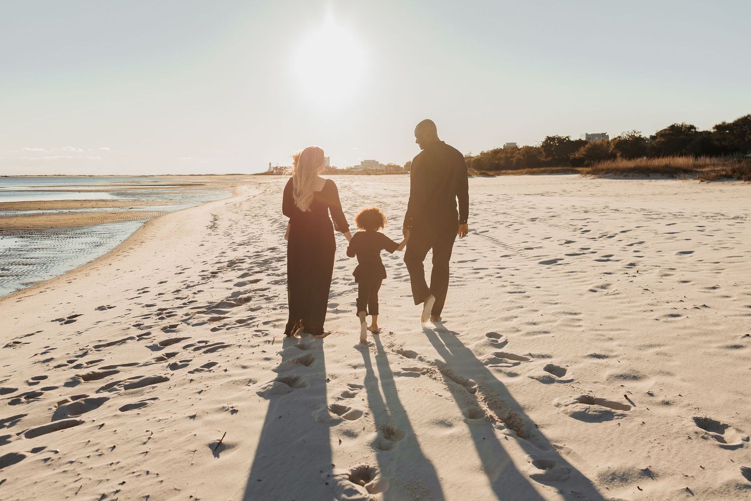 Family of four silhouetted against golden sunset light while strolling on beach.
