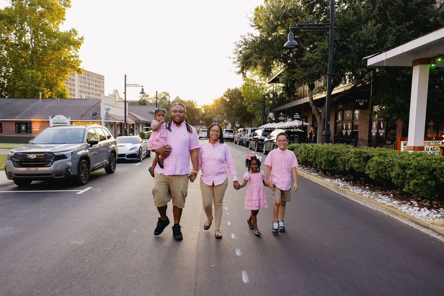 Family of five in matching pink outfits walking together on a sunny urban street at golden hour.