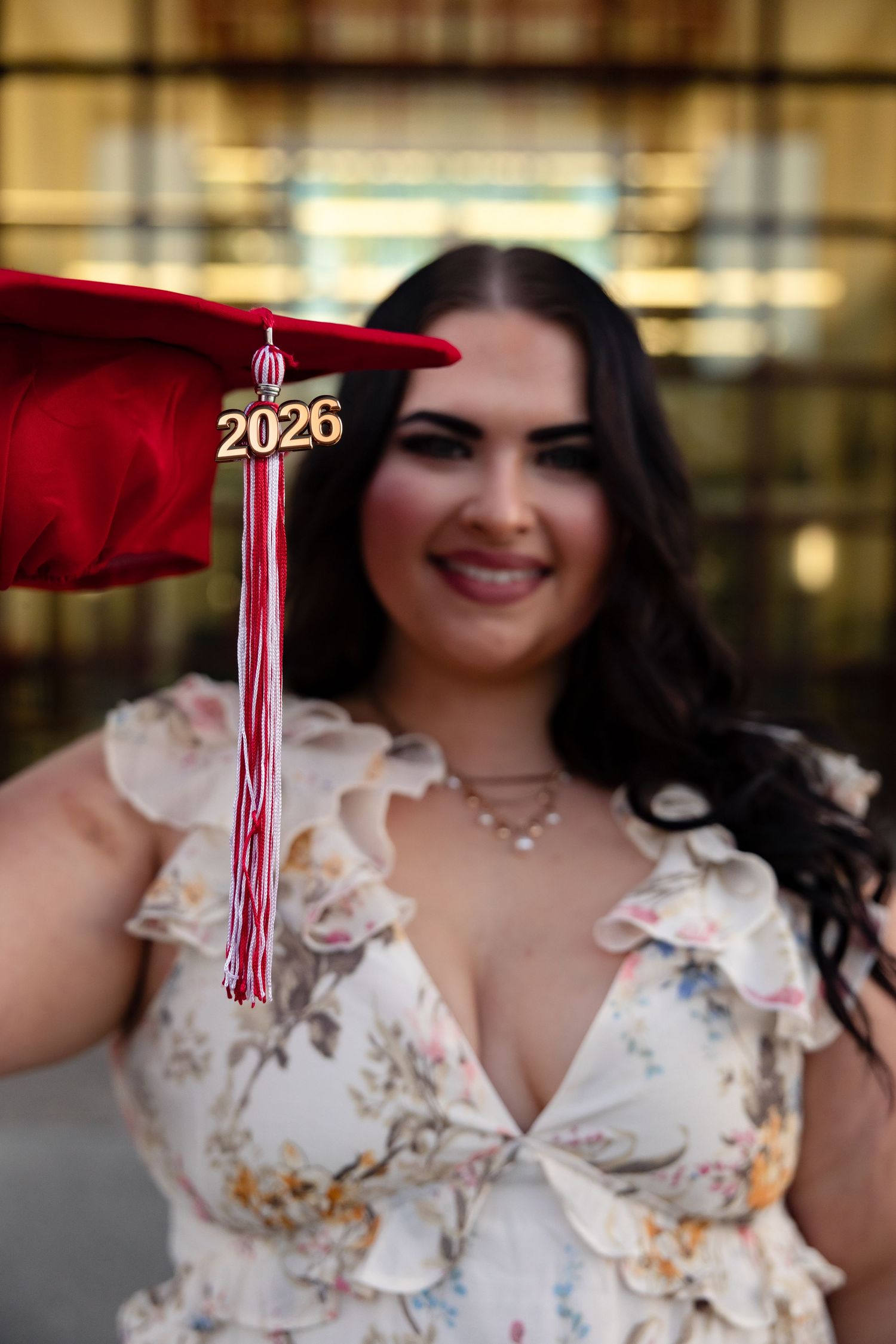 Close-up of red 2026 graduation cap held by smiling brunette in floral dress.