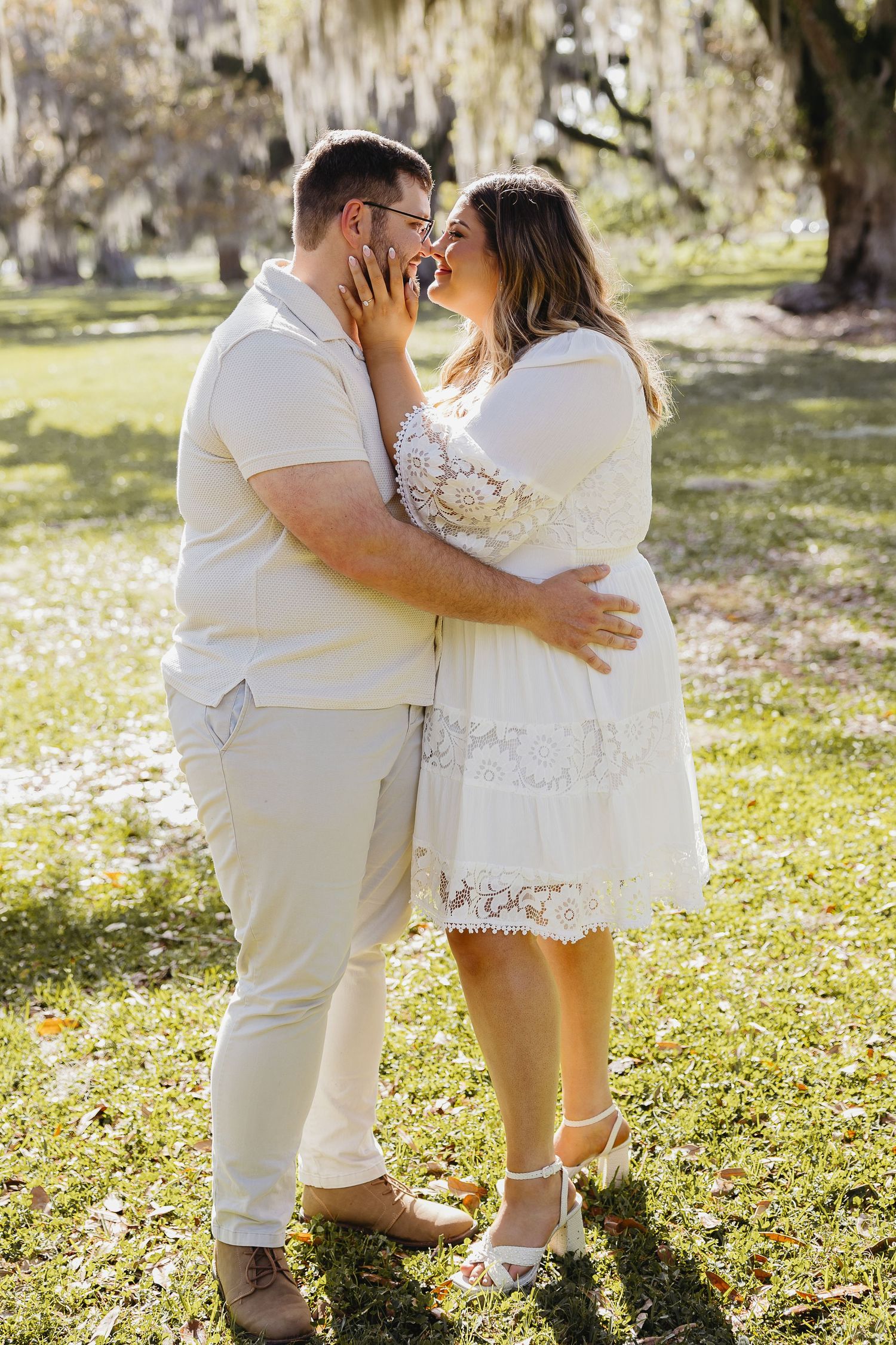 Engaged couple sharing a romantic almost-kiss embrace under Spanish moss trees outdoors.