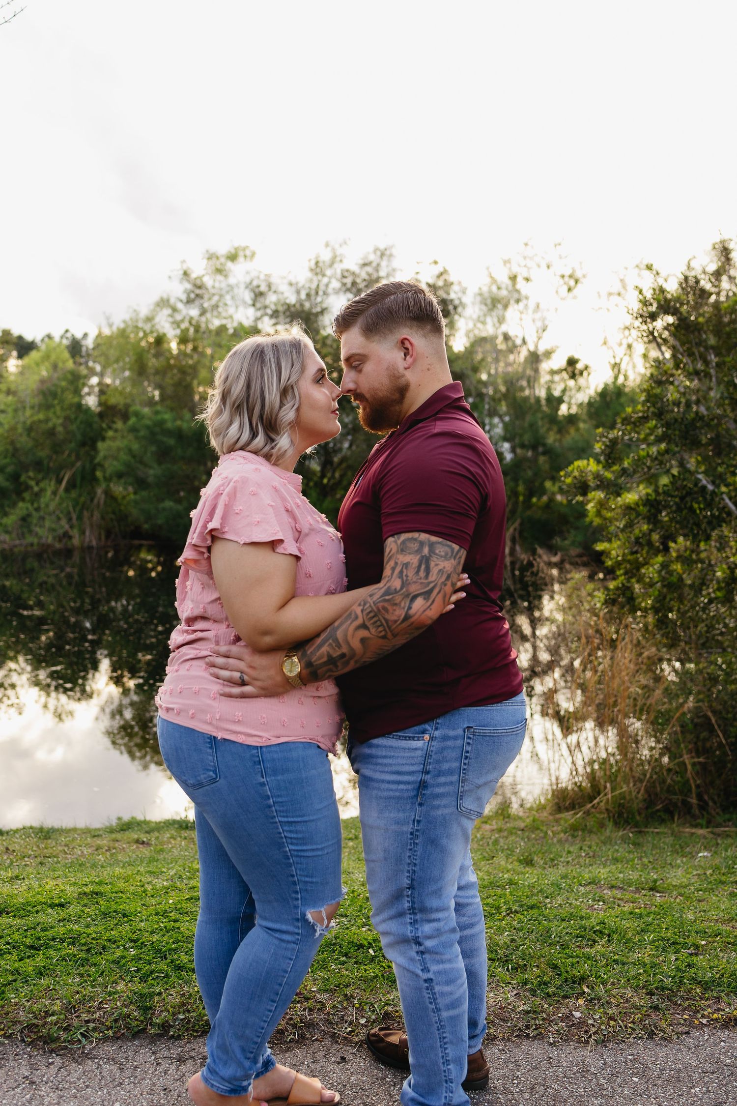 Couple sharing a romantic moment by a reflective pond, man with tattoos in maroon polo shirt.