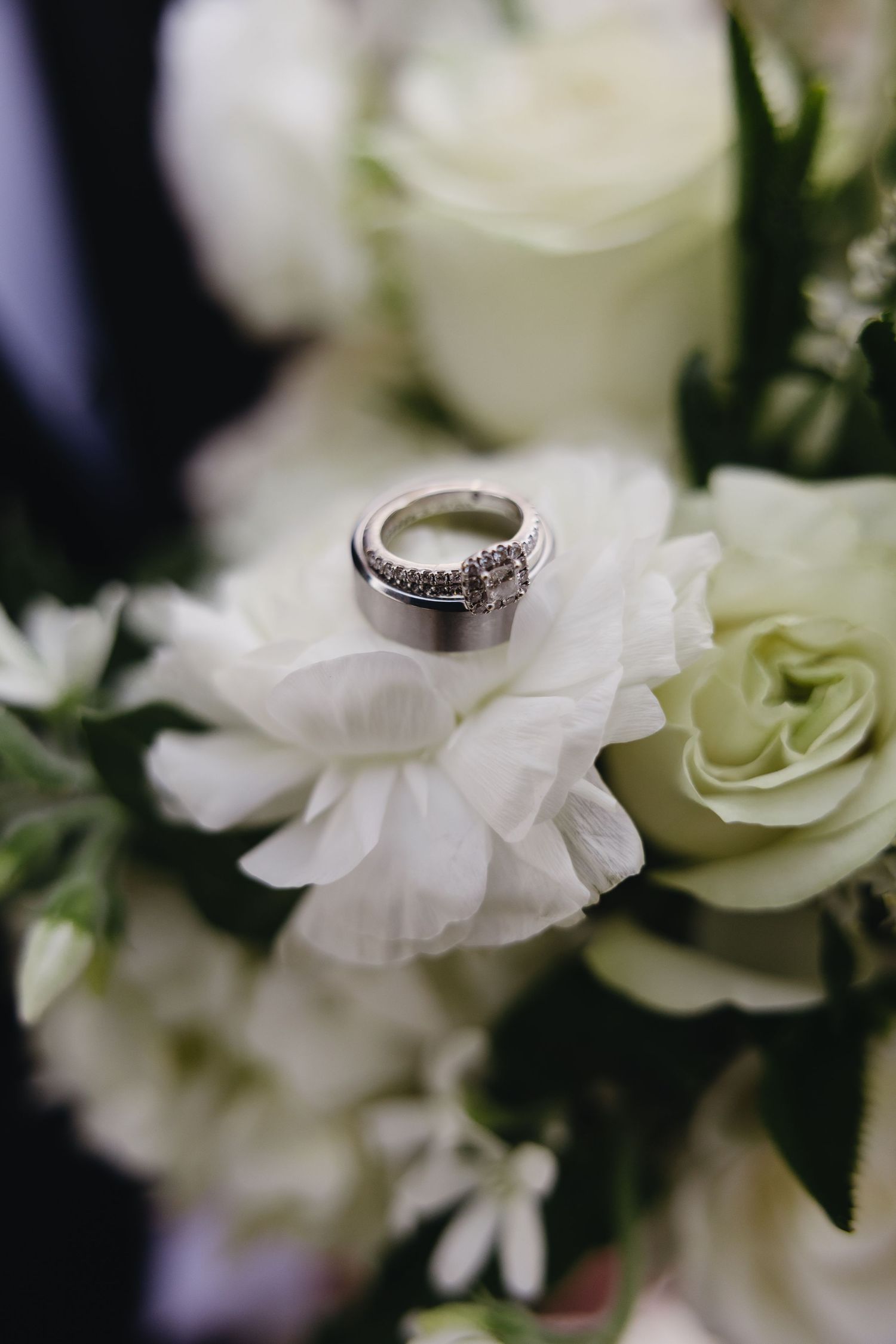 Wedding rings resting on white roses and flowers in a bridal bouquet close-up detail shot.
