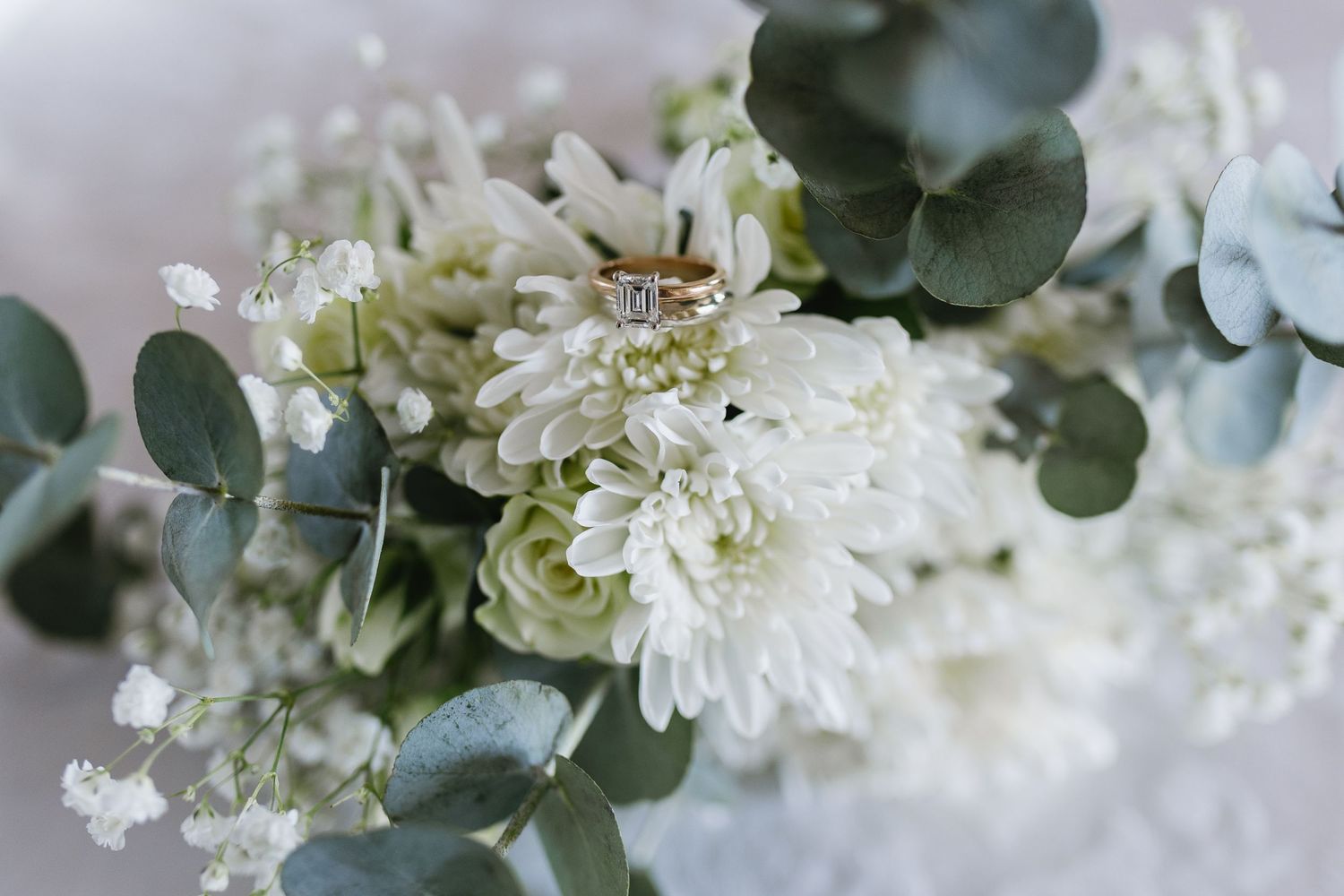 Elegant wedding ring resting on a white chrysanthemum and eucalyptus bridal bouquet.