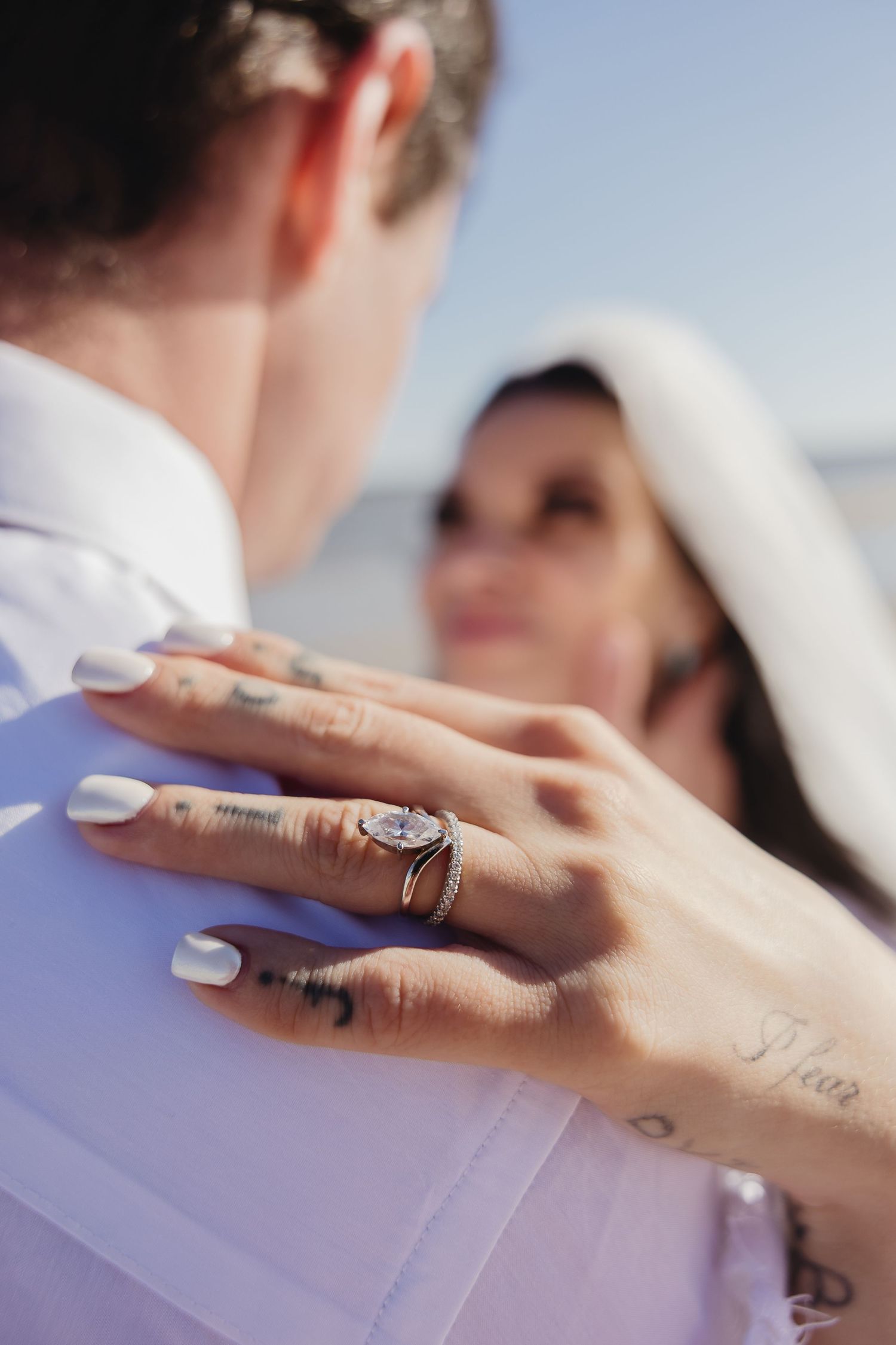 Close-up of bride's tattooed hand with diamond ring resting on groom's white shirt.