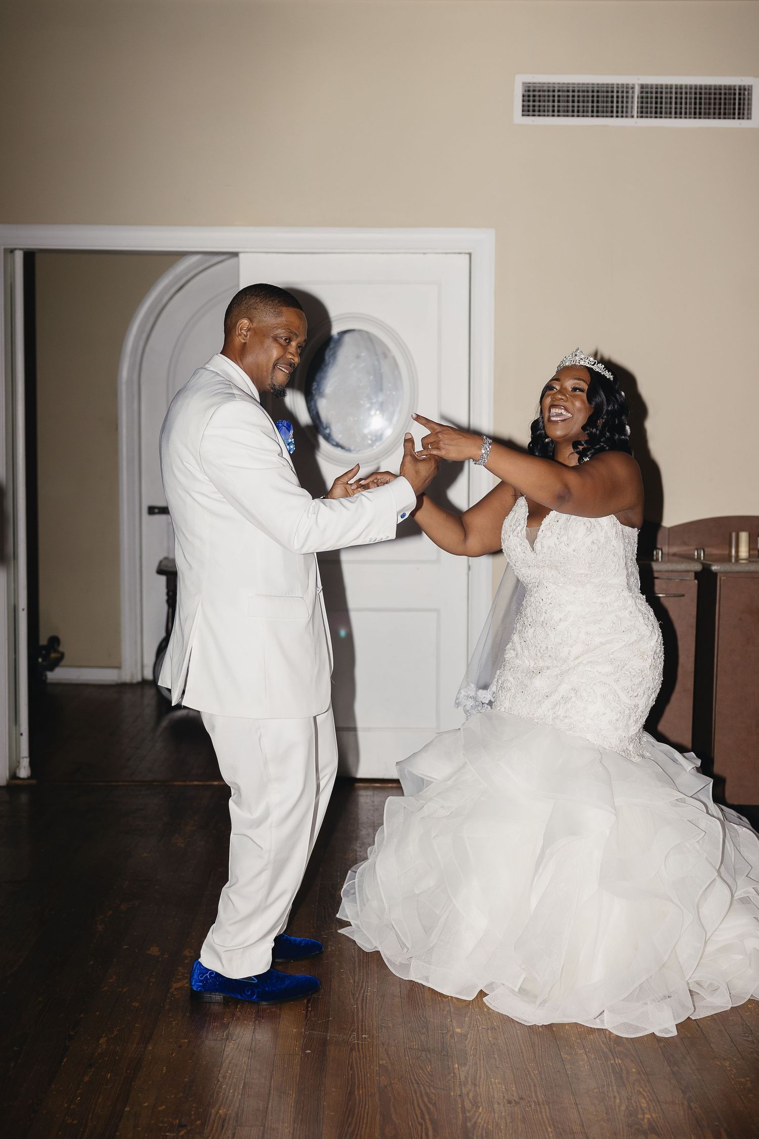 Joyful bride in mermaid gown and groom in white suit dancing together at wedding reception.