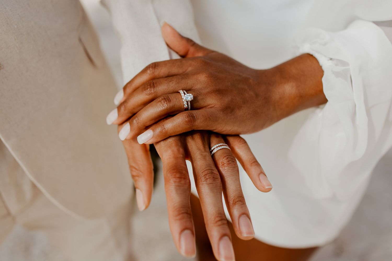 Close-up of newlyweds hands stacked together showing wedding rings and diamond engagement ring.