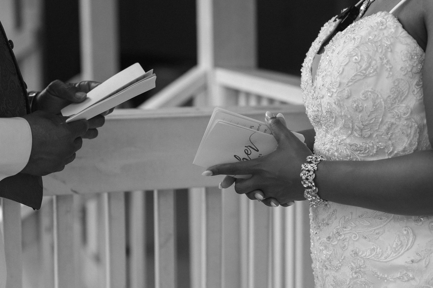Black and white close-up of bride and groom exchanging vows holding books at wedding.