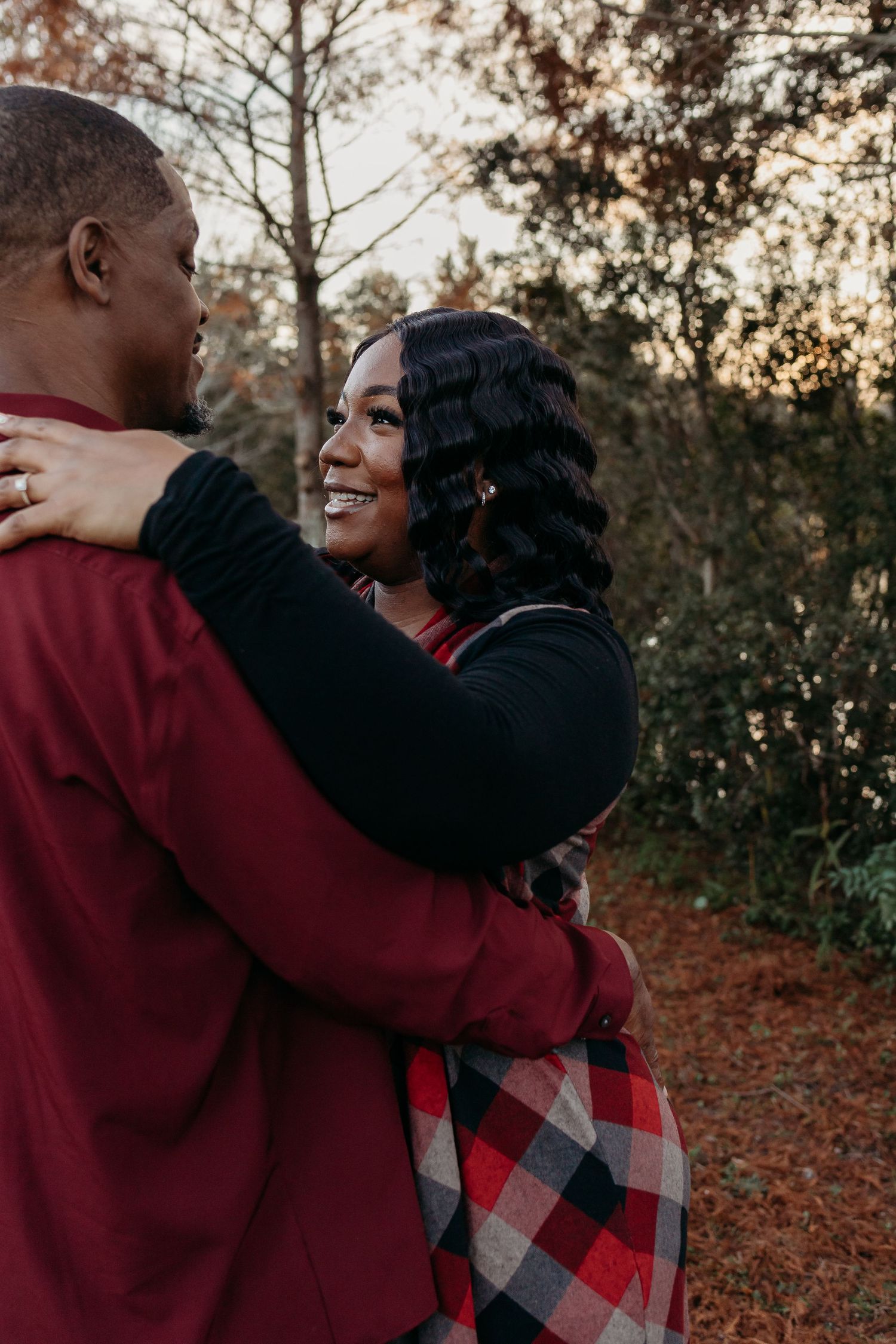 A joyful Black woman smiles warmly while embracing her partner outdoors in a fall forest setting.