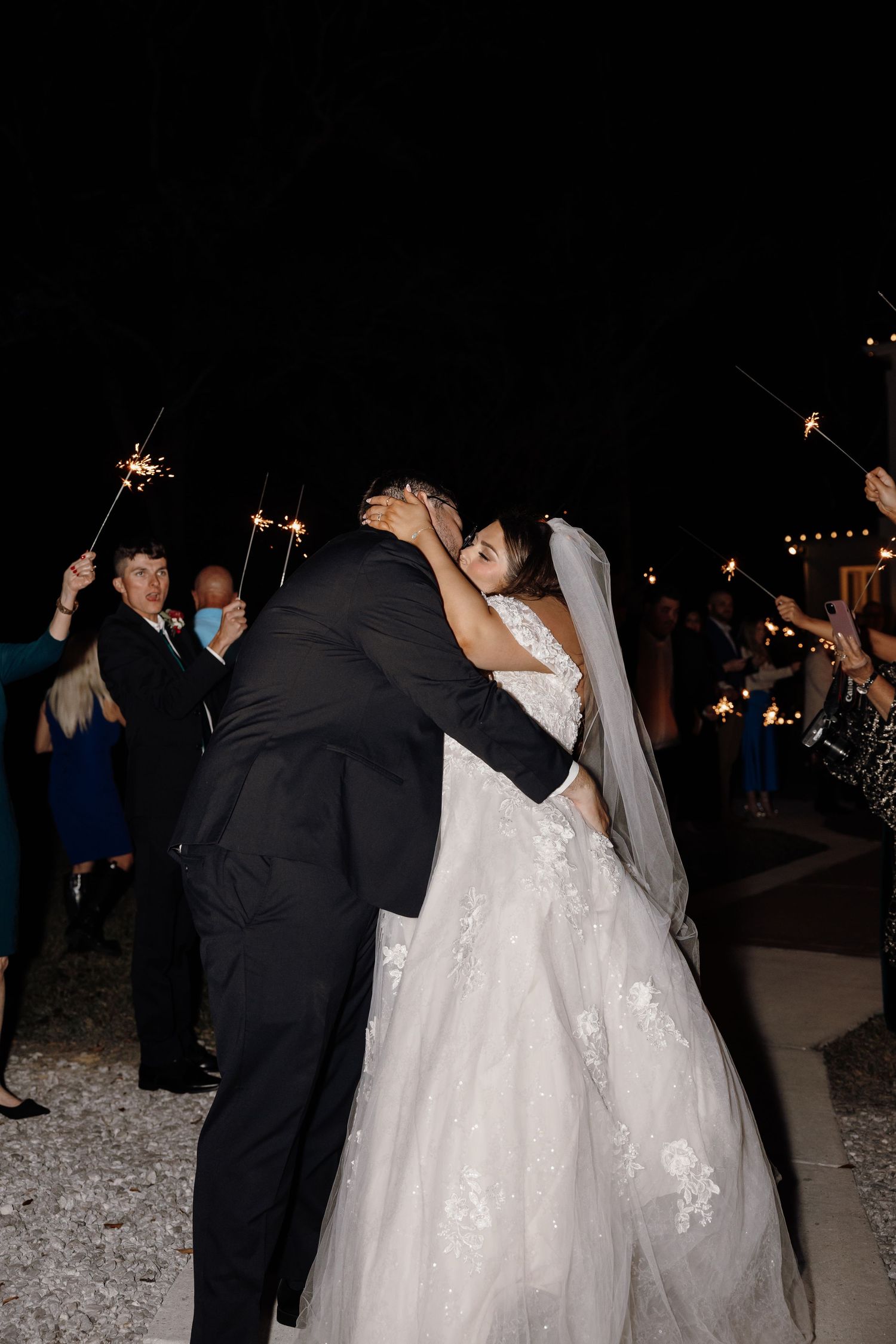 Bride and groom share a kiss surrounded by guests holding sparklers during their wedding send-off.