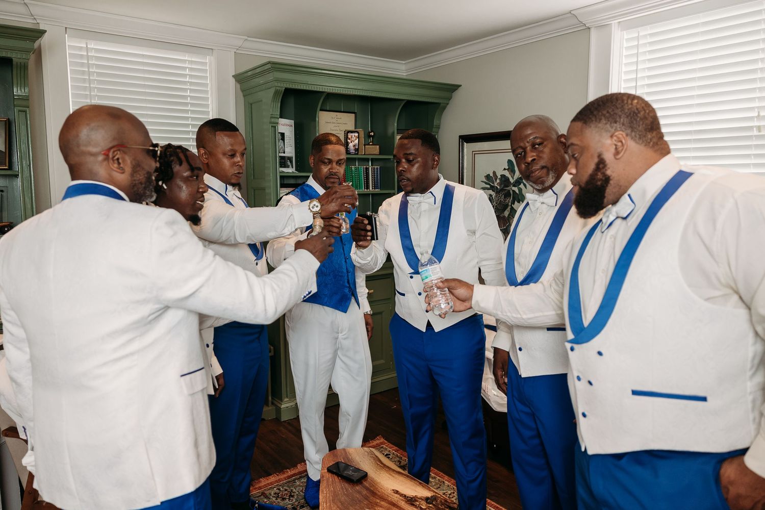 Groom and groomsmen in white and royal blue suits celebrating together before wedding ceremony.