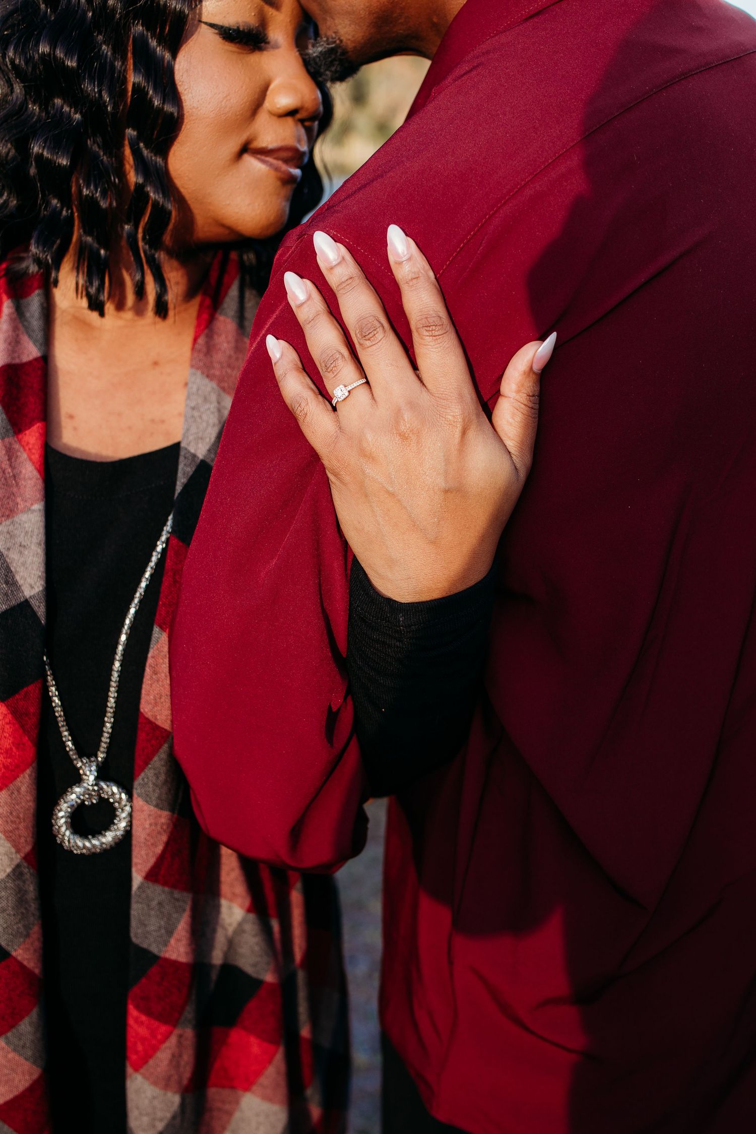 Close-up of a woman's hand with a ring resting on her partner's red jacket during a romantic embrace.