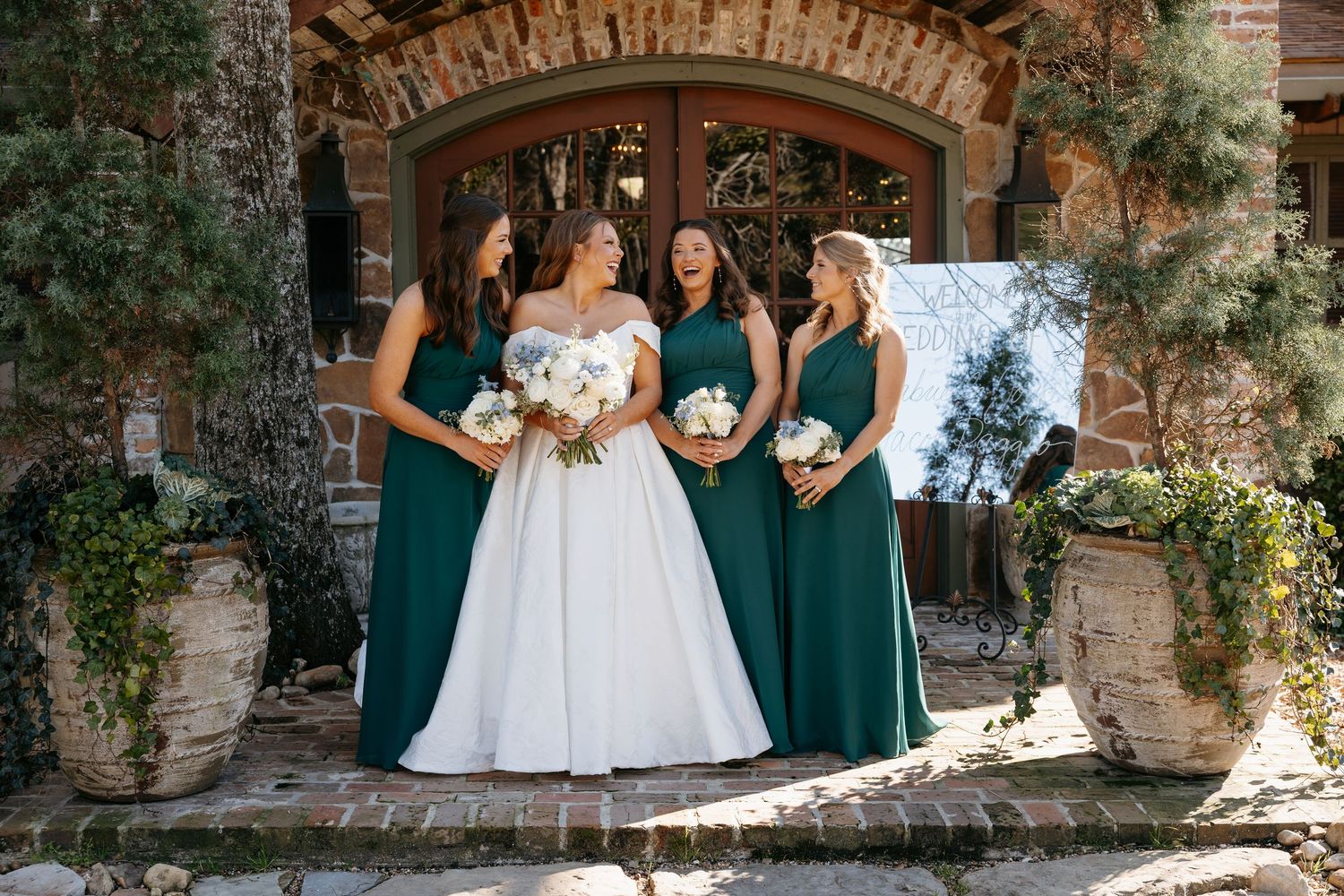 Bride in white ballgown poses with three bridesmaids in emerald green gowns holding white bouquets.