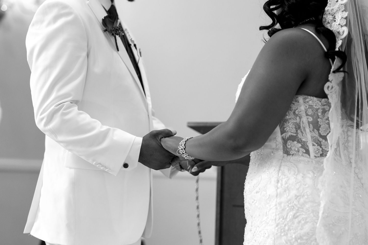 Black and white photo of bride and groom holding hands at the wedding altar.