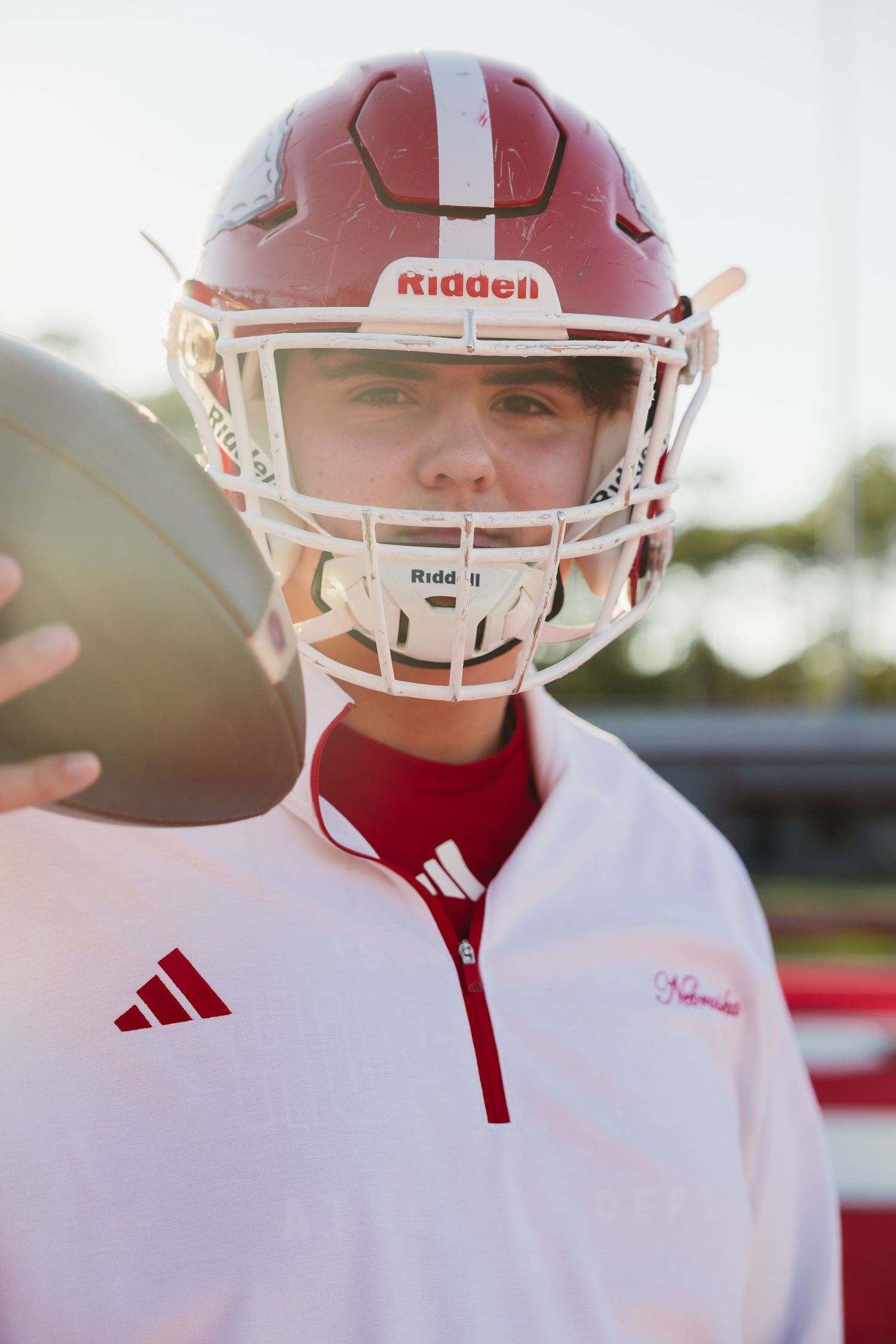 Close-up portrait of young football player in red Riddell helmet holding ball.