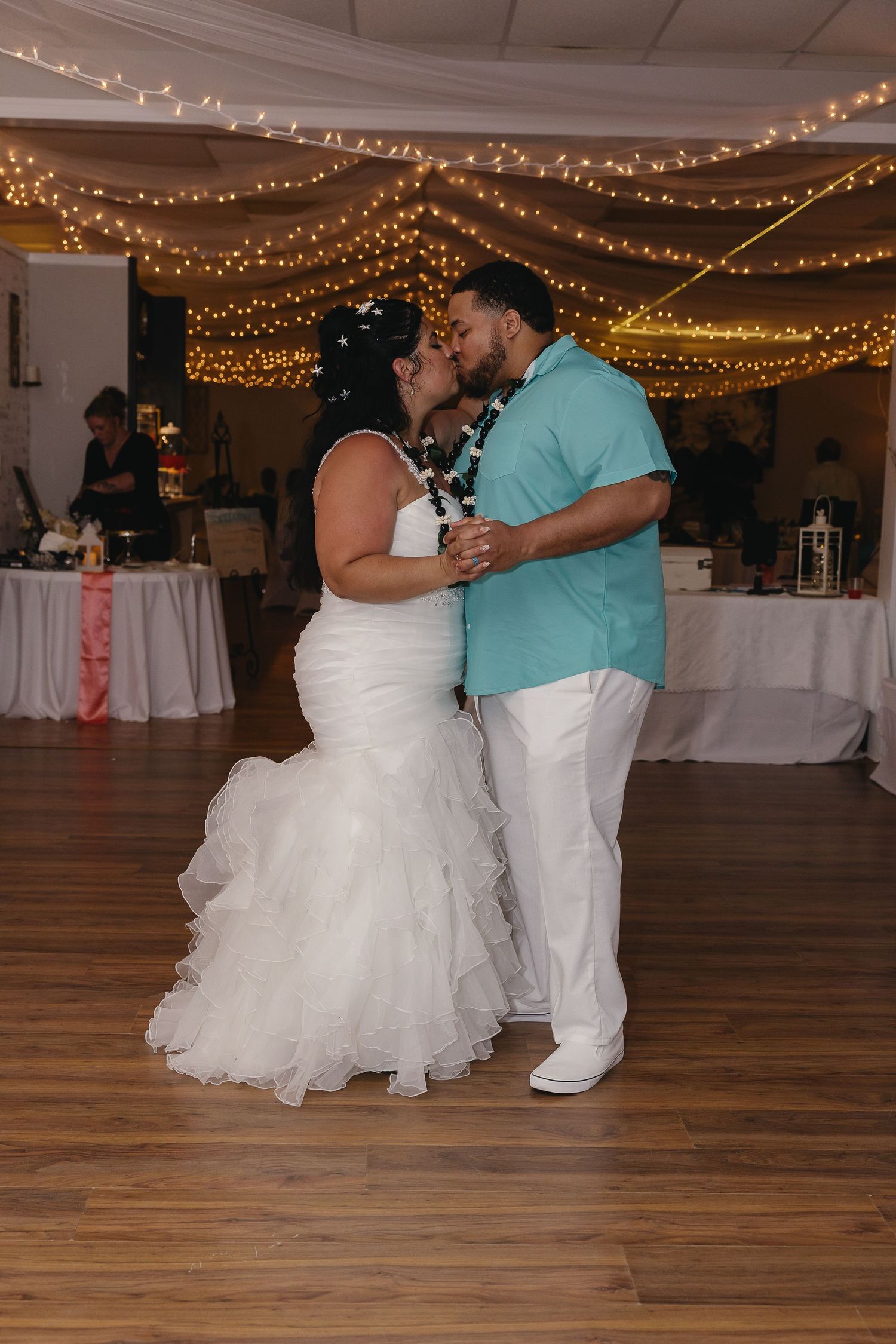 Bride and groom share first dance kiss under romantic string lights at wedding reception.