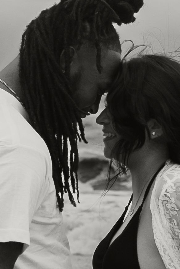 Intimate black and white portrait of couple leaning foreheads together on windy beach.