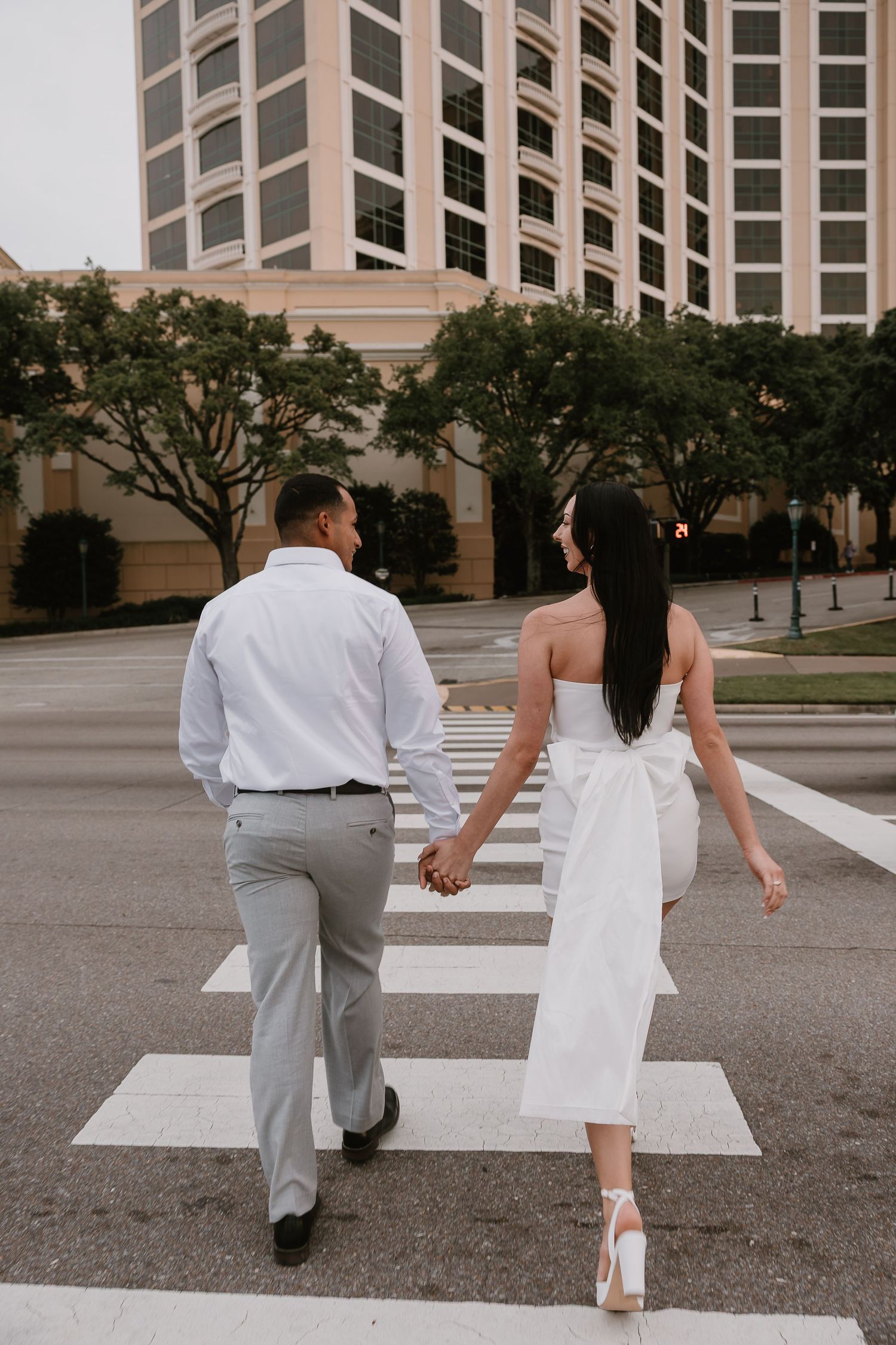 Couple holding hands while crossing a zebra crosswalk in an urban setting during their engagement session.