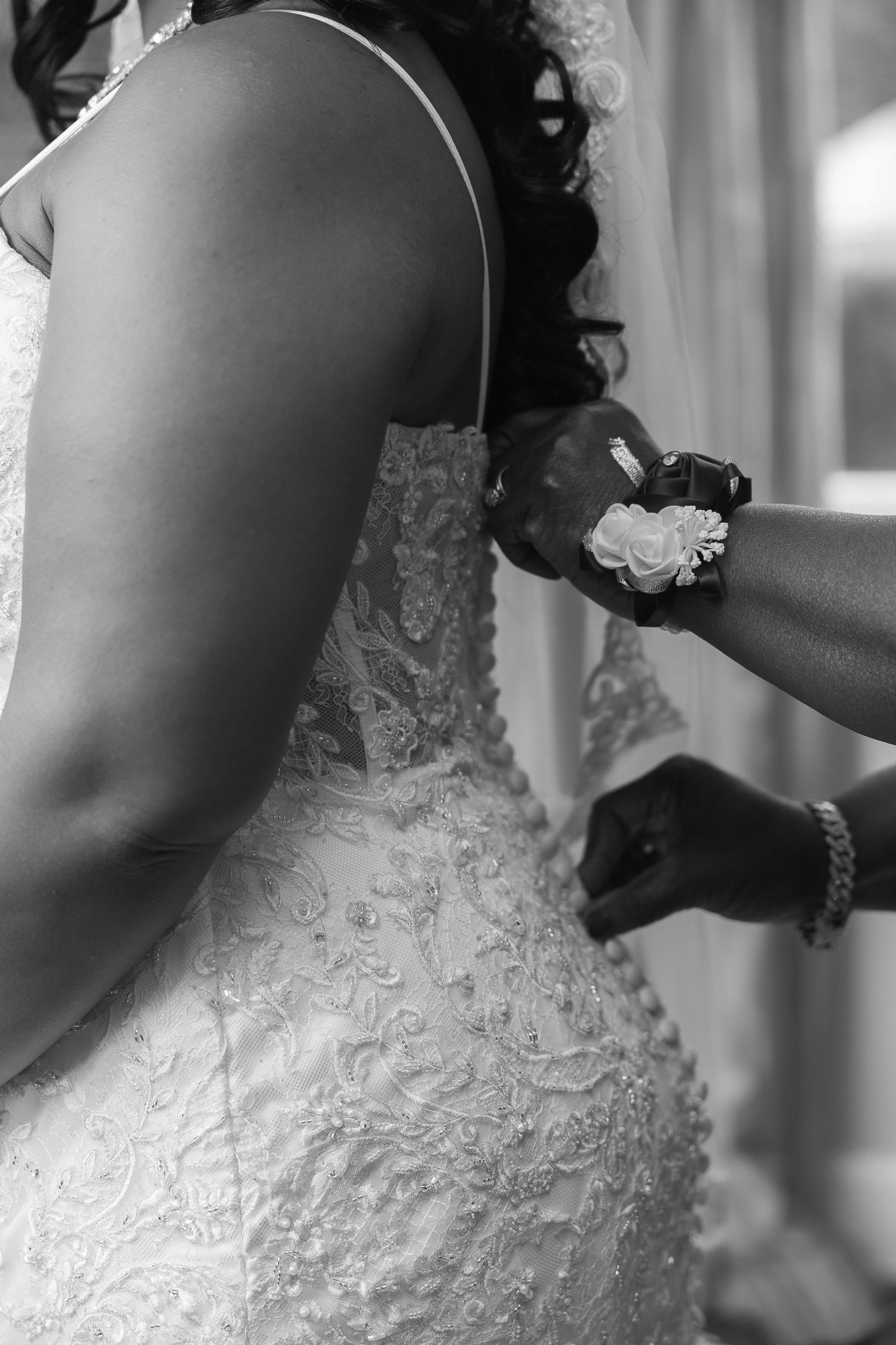 Black and white close-up of bride having her lace wedding dress fastened by an assistant.